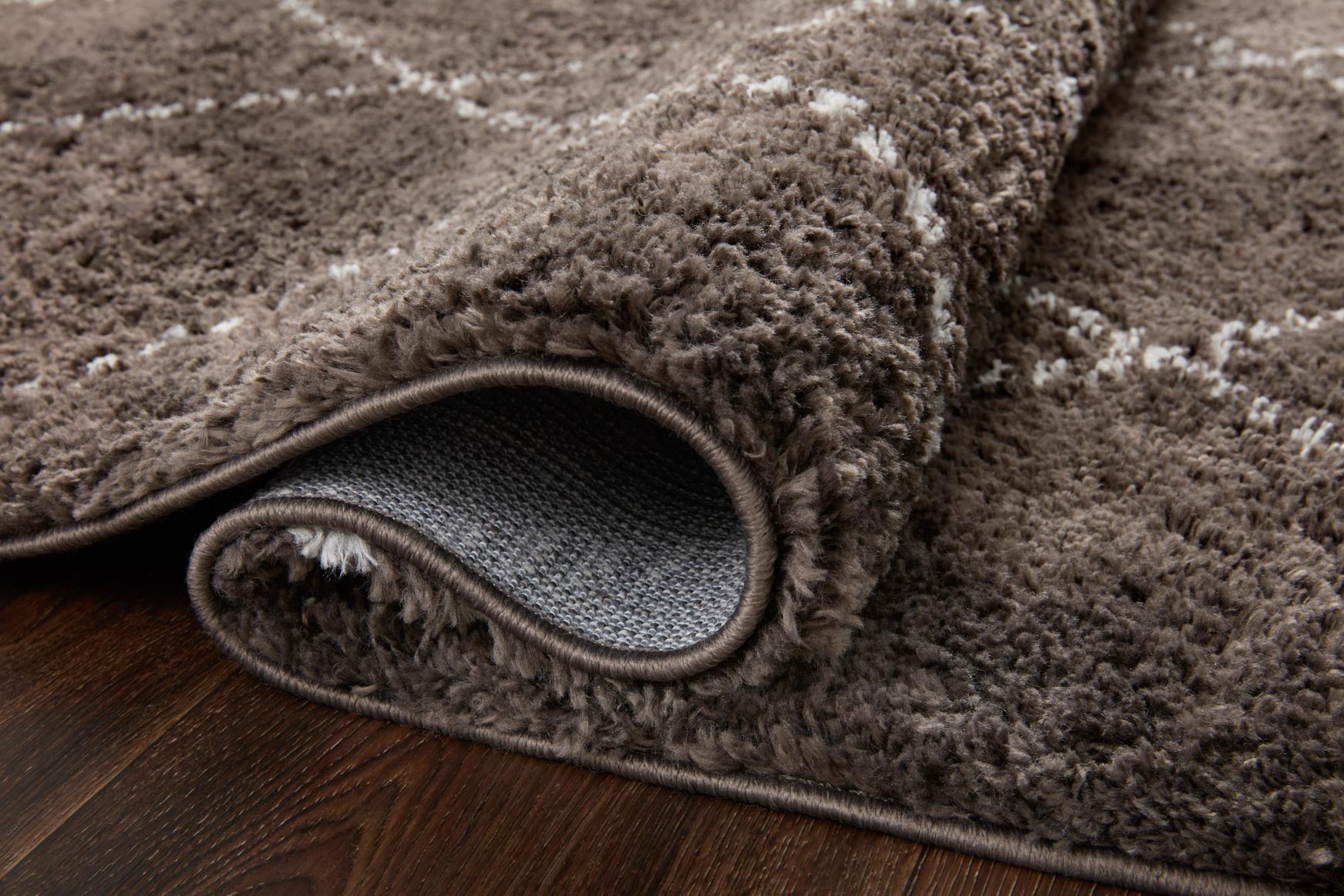 Dark shag rug corner with stitched edge and light grey diamond pattern.