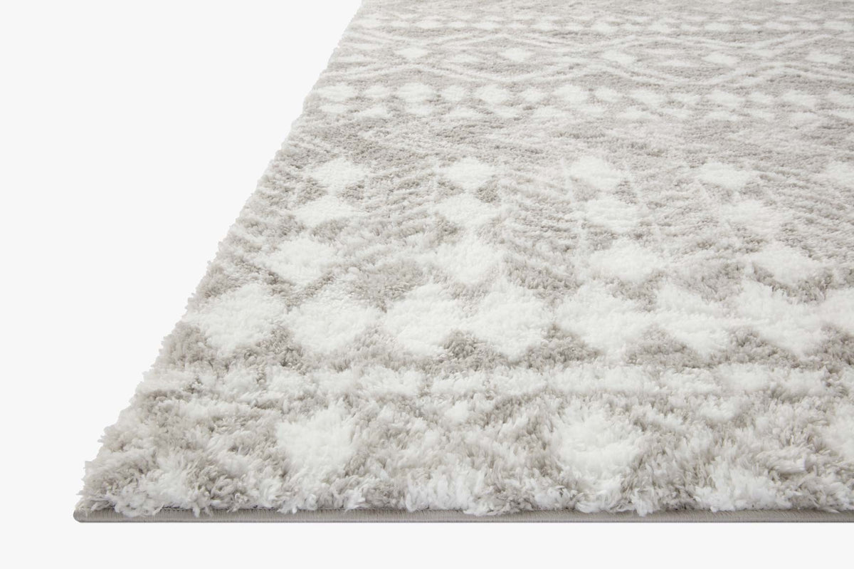 Grey and white shag rug corner with dense high pile and geometric motif.