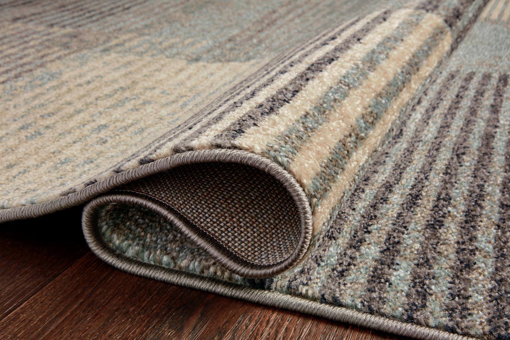 Rolled edge of storm-and-taupe abstract rug with bound border and stripe texture