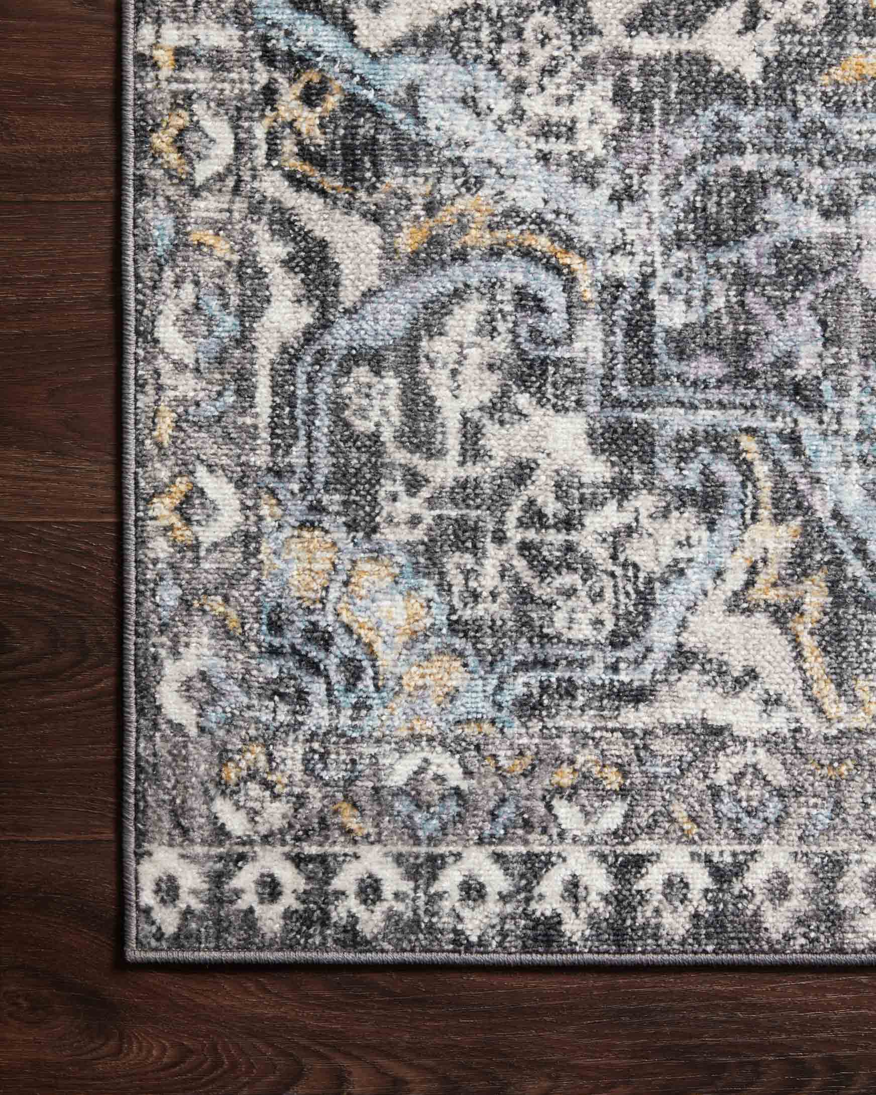 Charcoal area rug with ornate geometric pattern and gold highlights, corner view