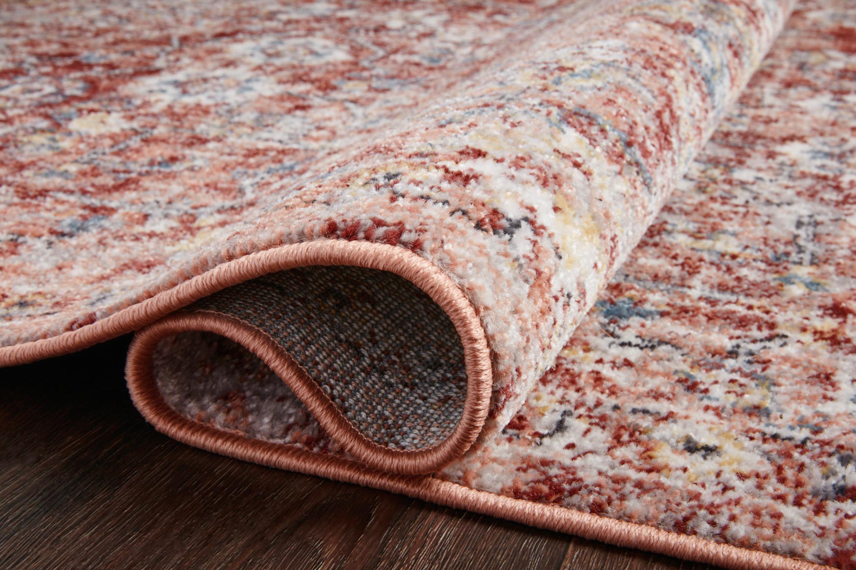Rug edge close-up showing rust and ivory tones with a stitched border and low pile.