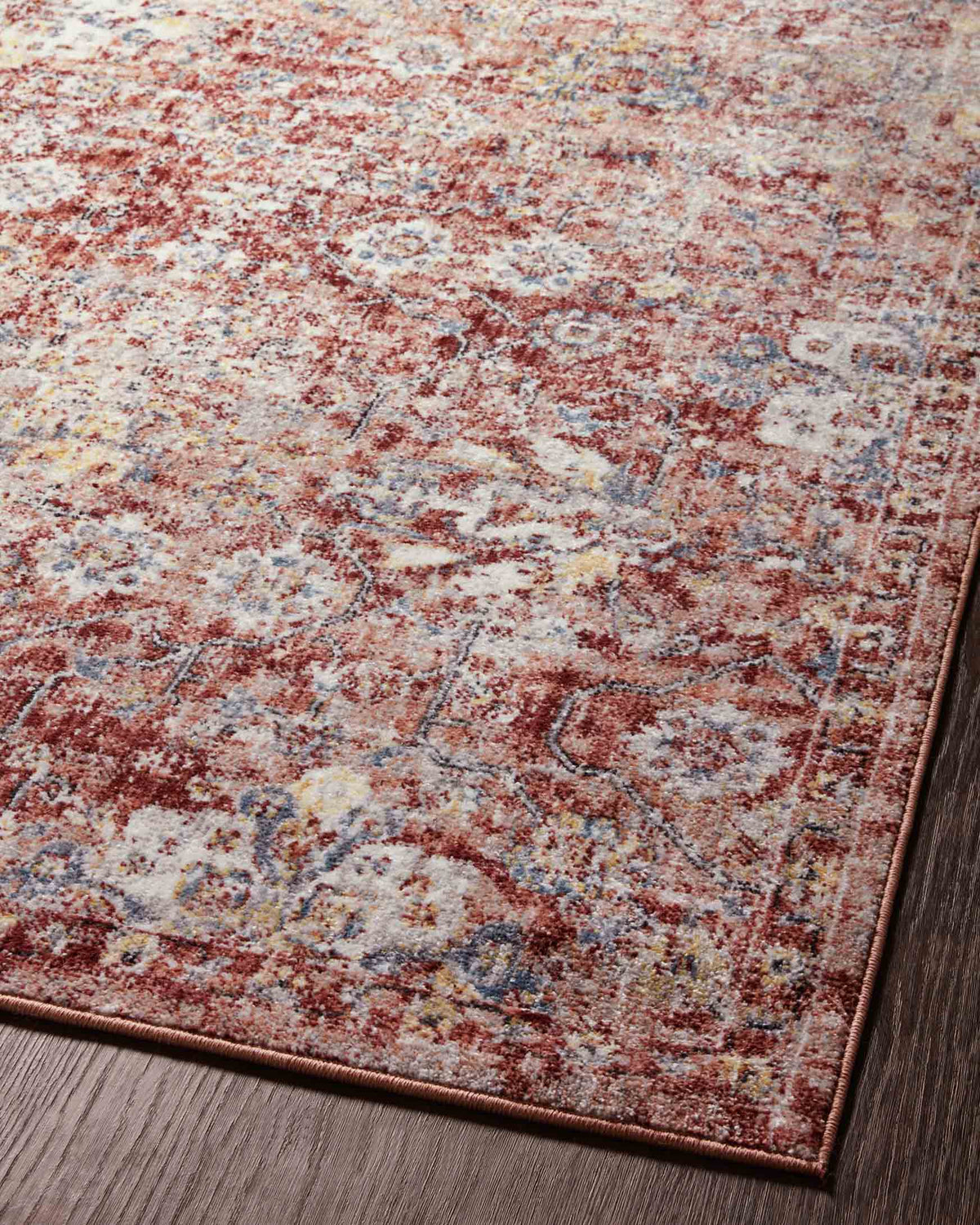 Top-left area close-up of rust and ivory traditional power loomed rug on dark wood floor.