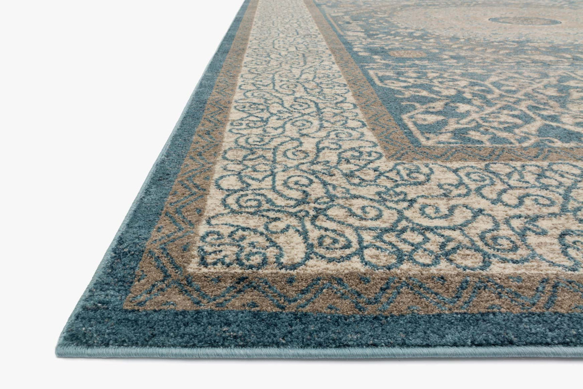 Angle view of blue and sand patterned power-loomed rug with ornate border edge.