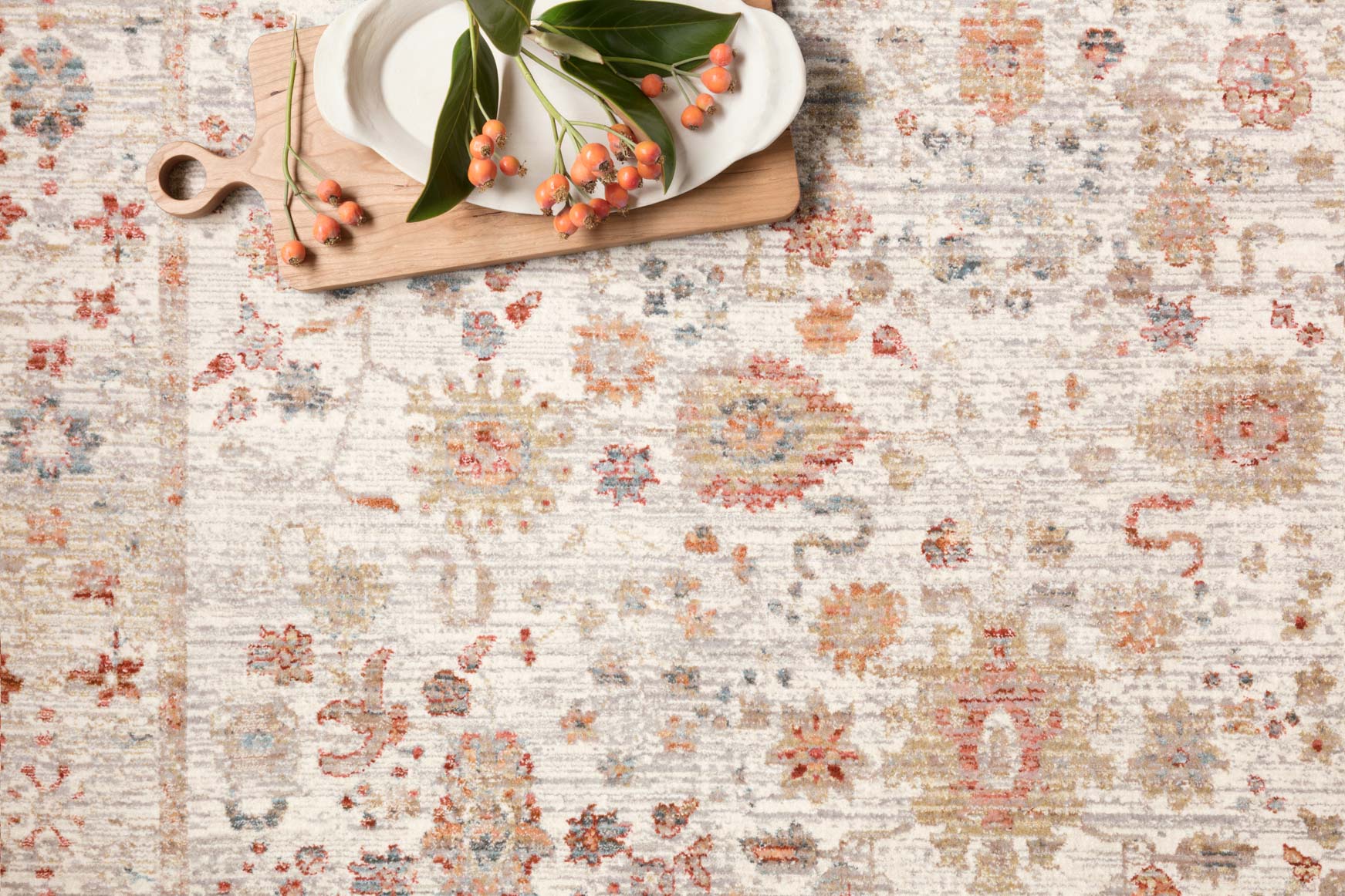 Ivory rug close-up with distressed floral and geometric motifs in red, blue, and tan.