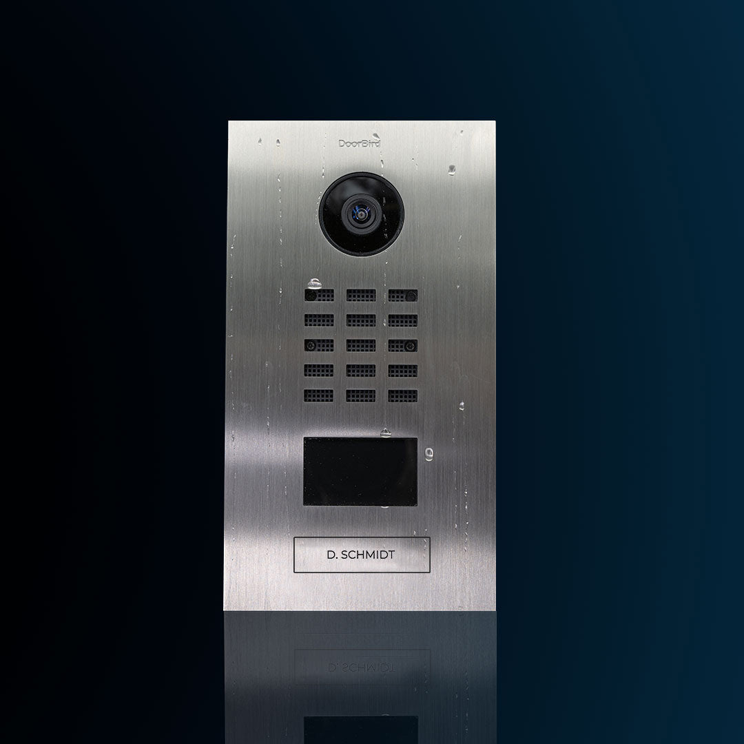 Stainless steel video door station with camera lens, keypad grid, and display window.