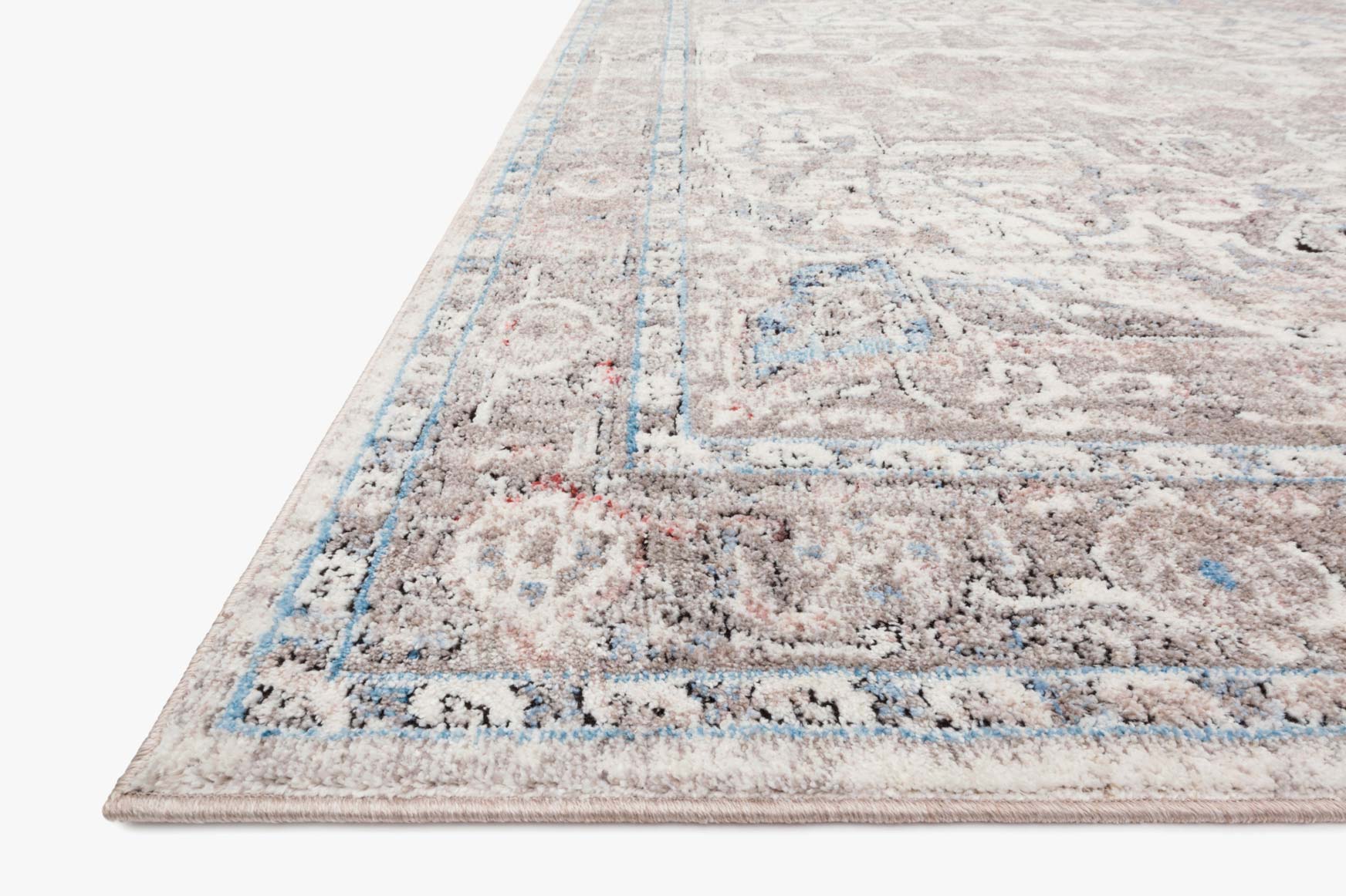 Close-up of ivory and stone rug with ornate motifs and distressed blue border lines.