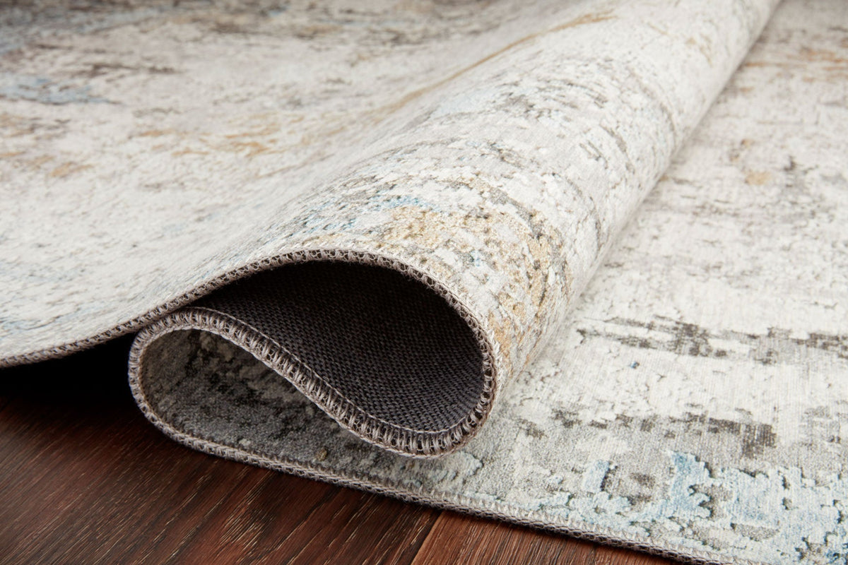 Rolled edge of antique rug showing light gray and blue distressed pile underside