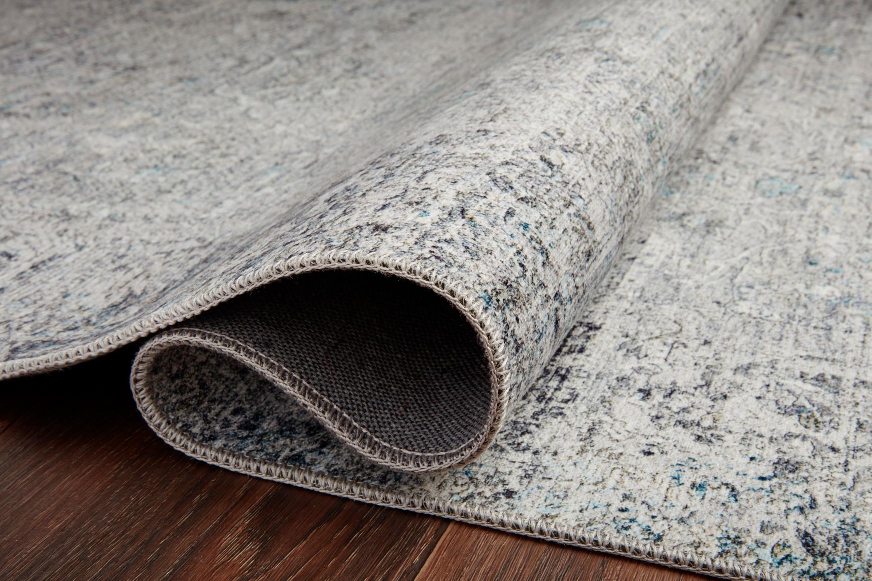 Ivory and silver rug with low pile and bound border; close-up of rolled edge.