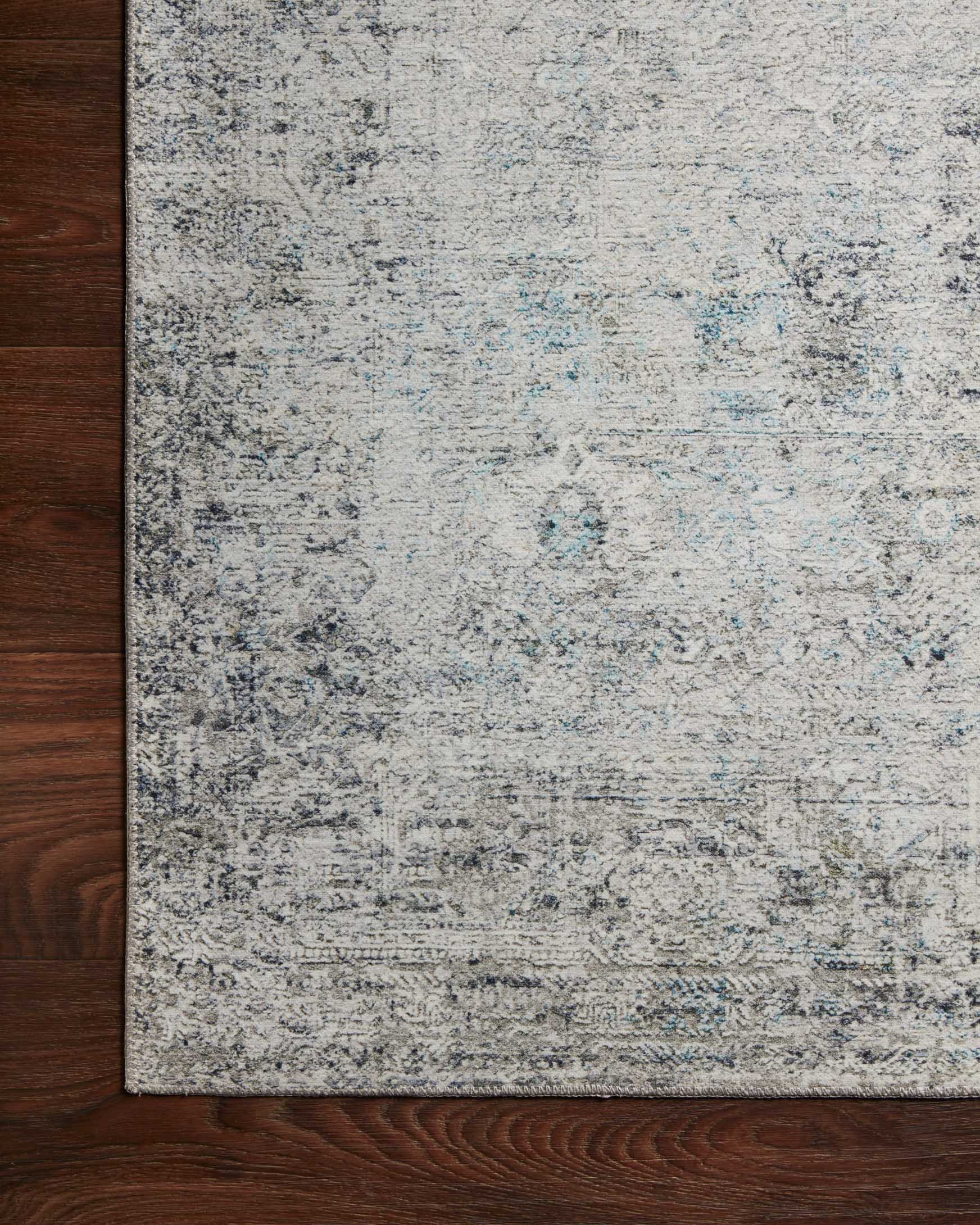 Corner view of an ivory and silver rug with distressed abstract design and flat pile.