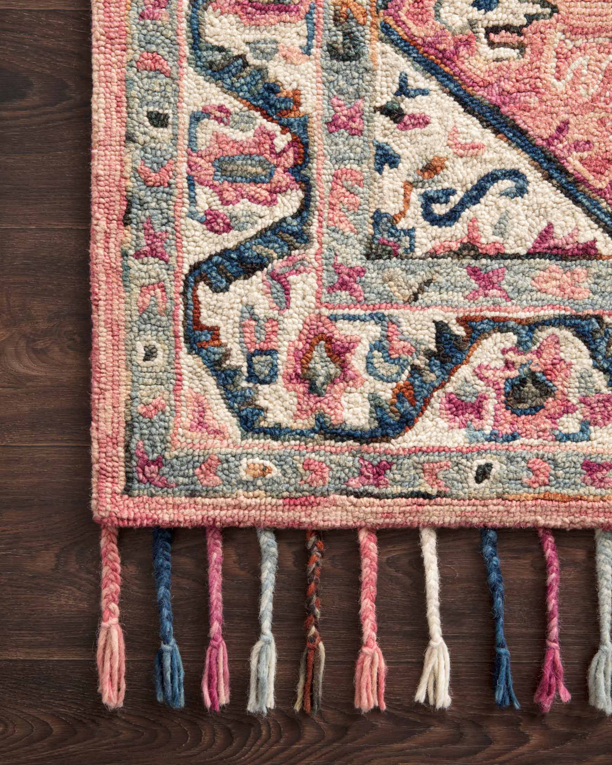 Border detail of pink, blue, and cream hooked rug with patterned trim and multicolor fringe