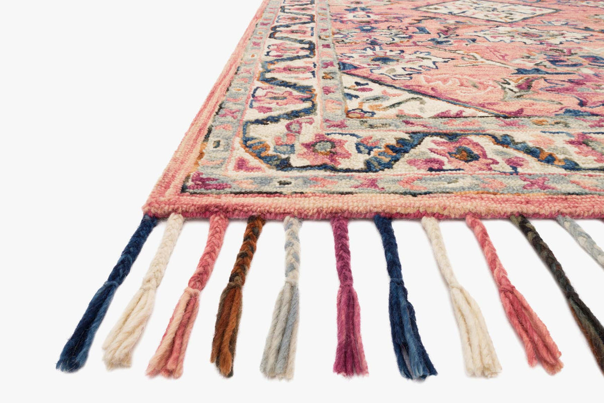 Corner view of pink, blue, and cream hooked rug with geometric pattern and multicolor fringe