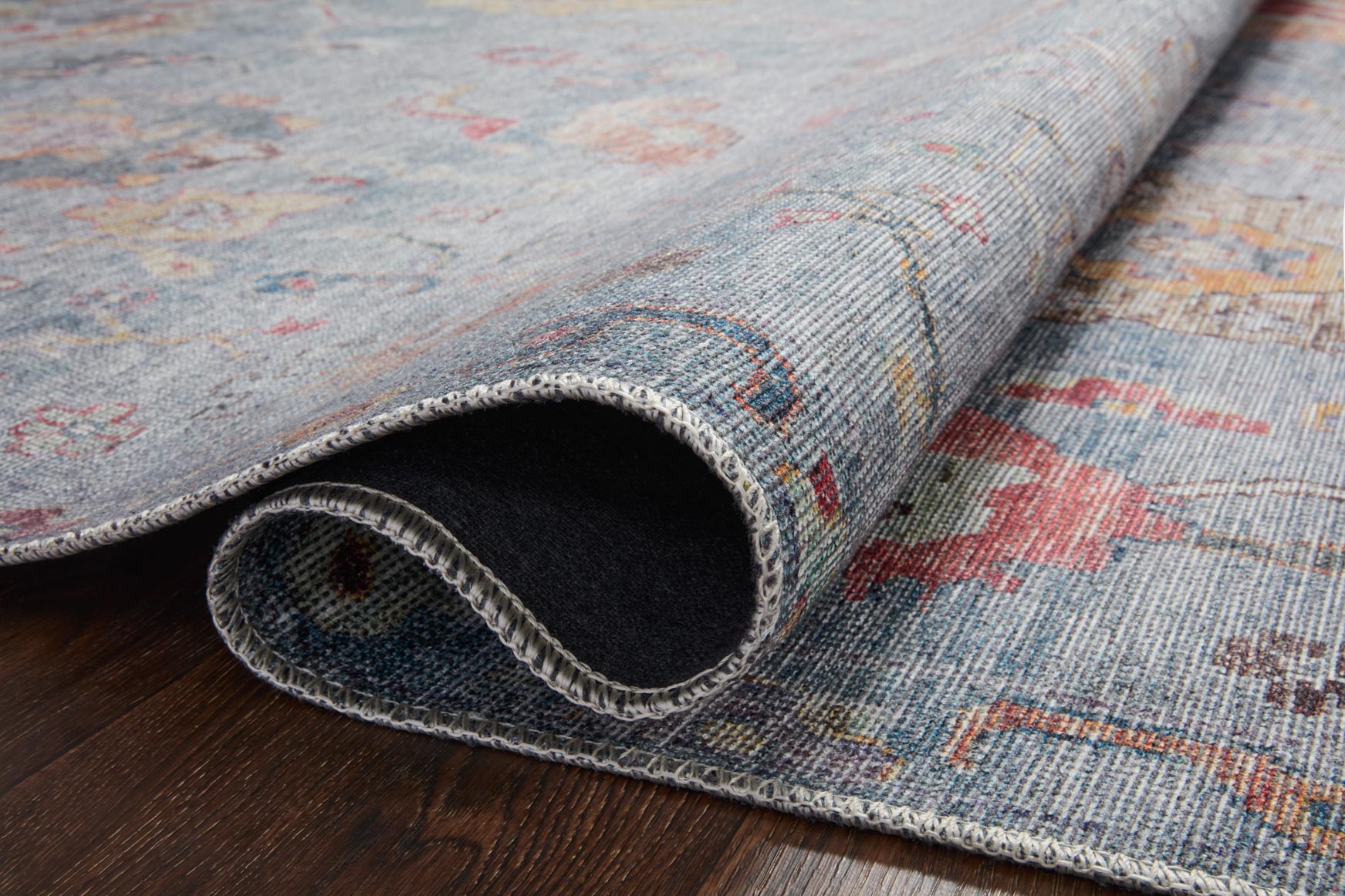 Rolled edge view of denim blue rug showing dark backing and stitched border