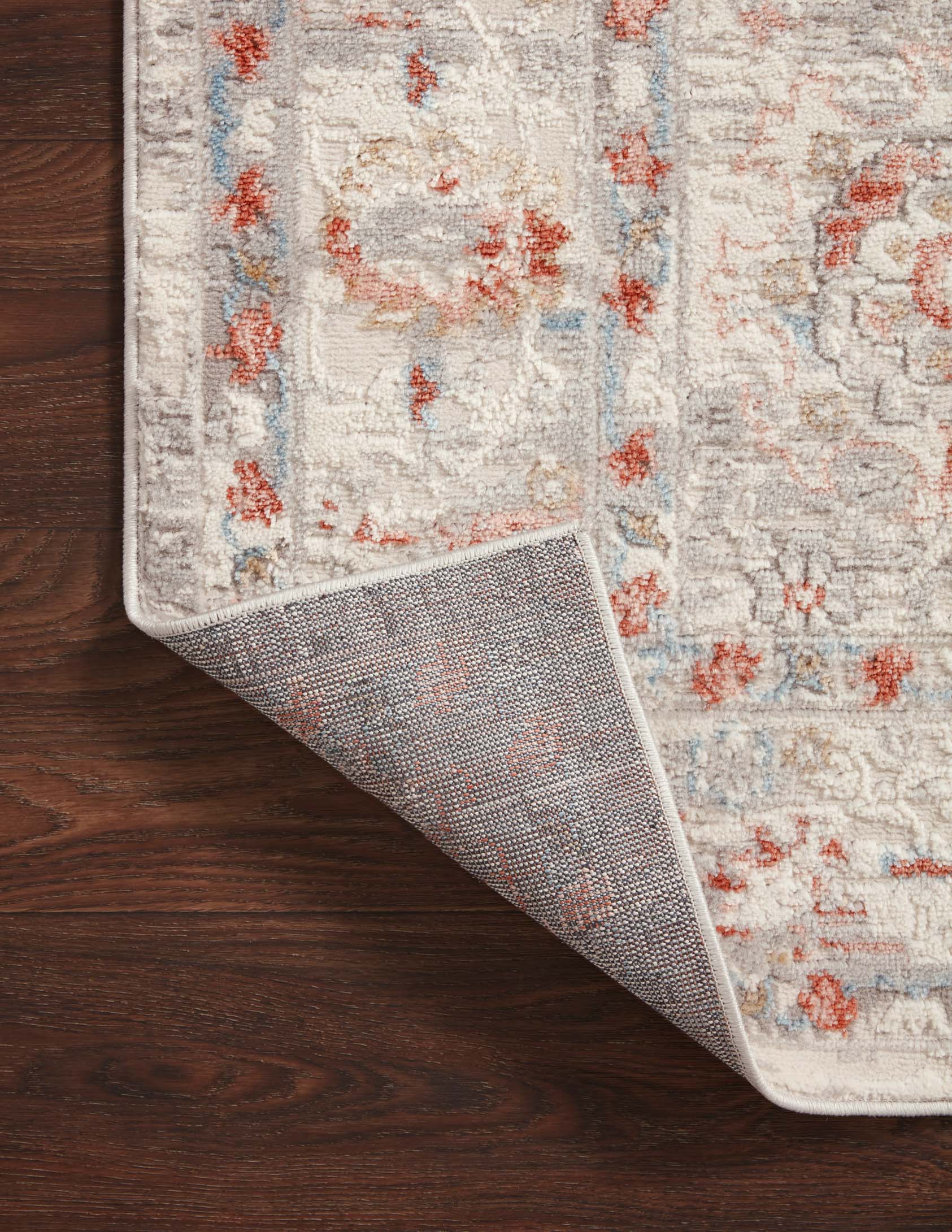 Ivory transitional rug showing rust and blue motif; corner rolled for detail