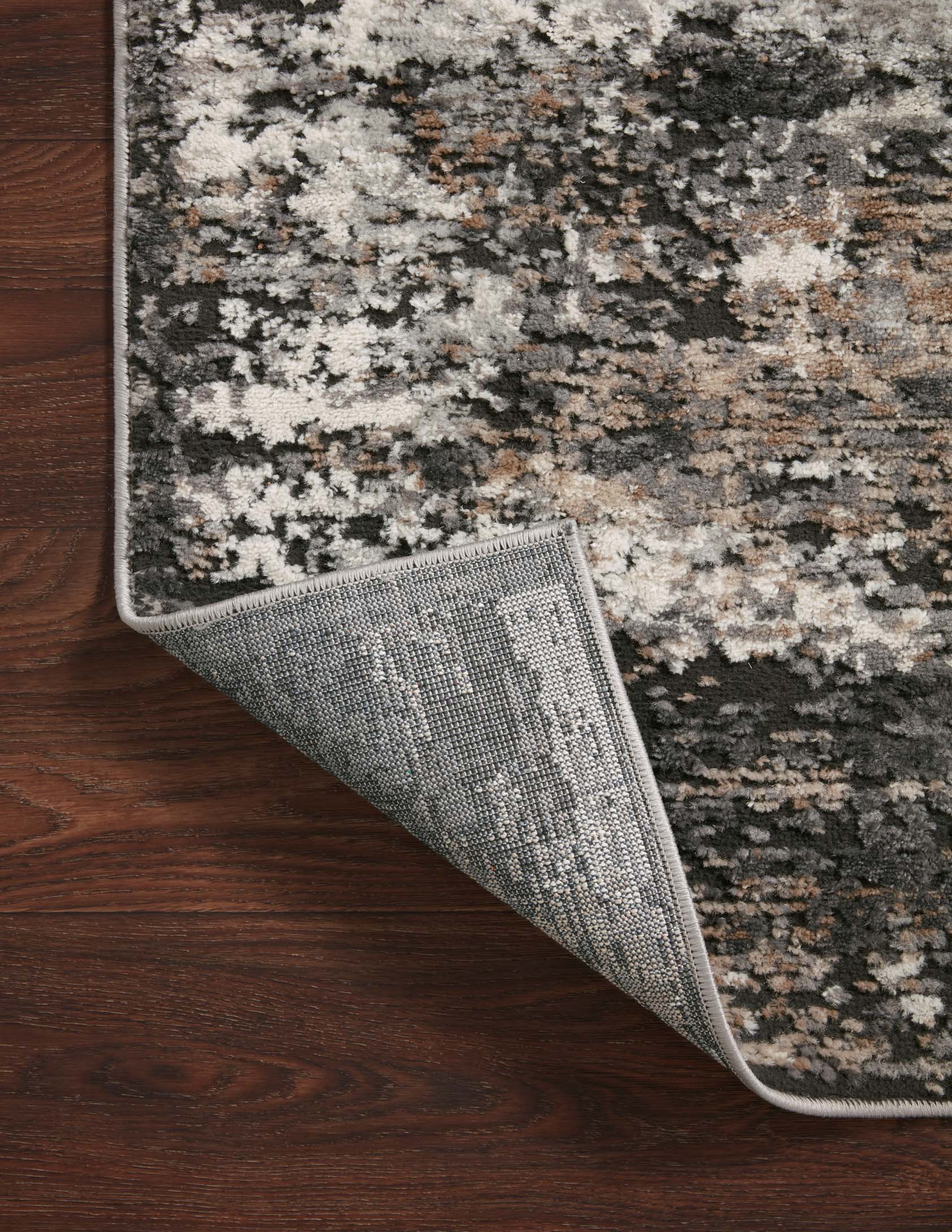 Textured charcoal and granite rug corner with rolled edge and visible woven backing underside.