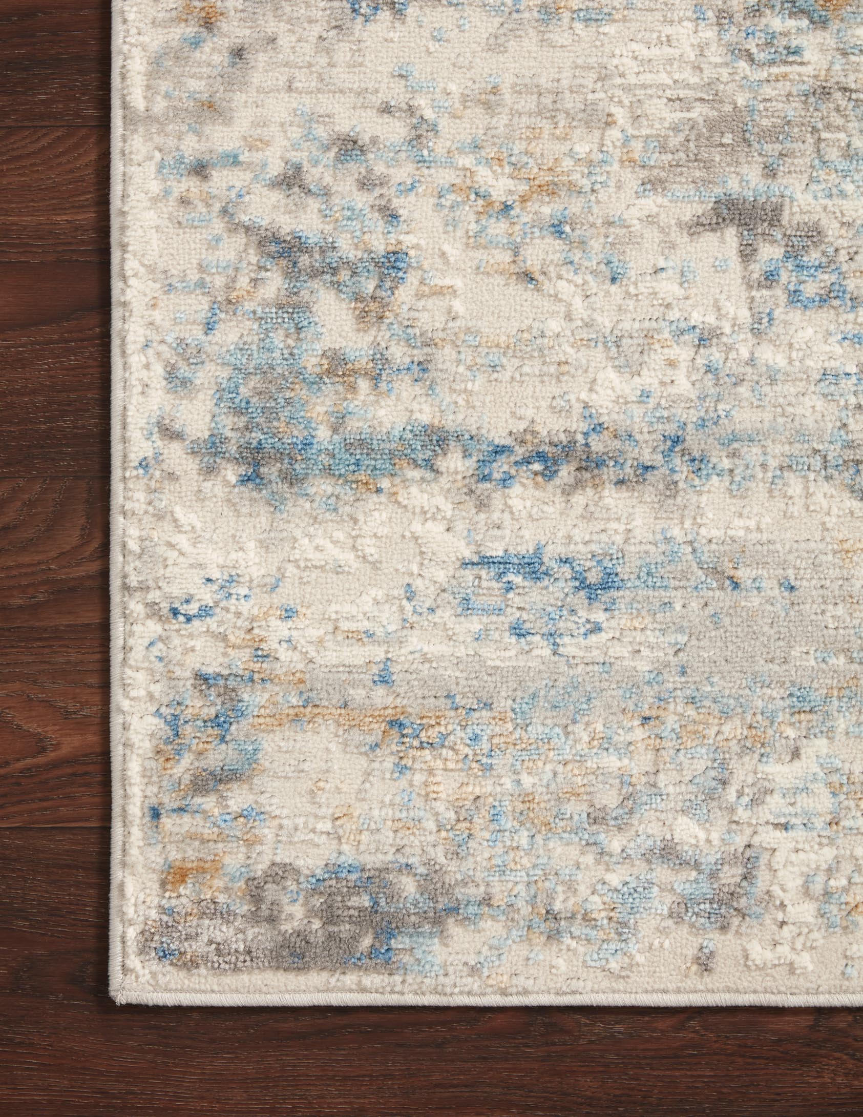 Ivory and ocean area rug corner on dark wood floor, showing abstract distressed weave.