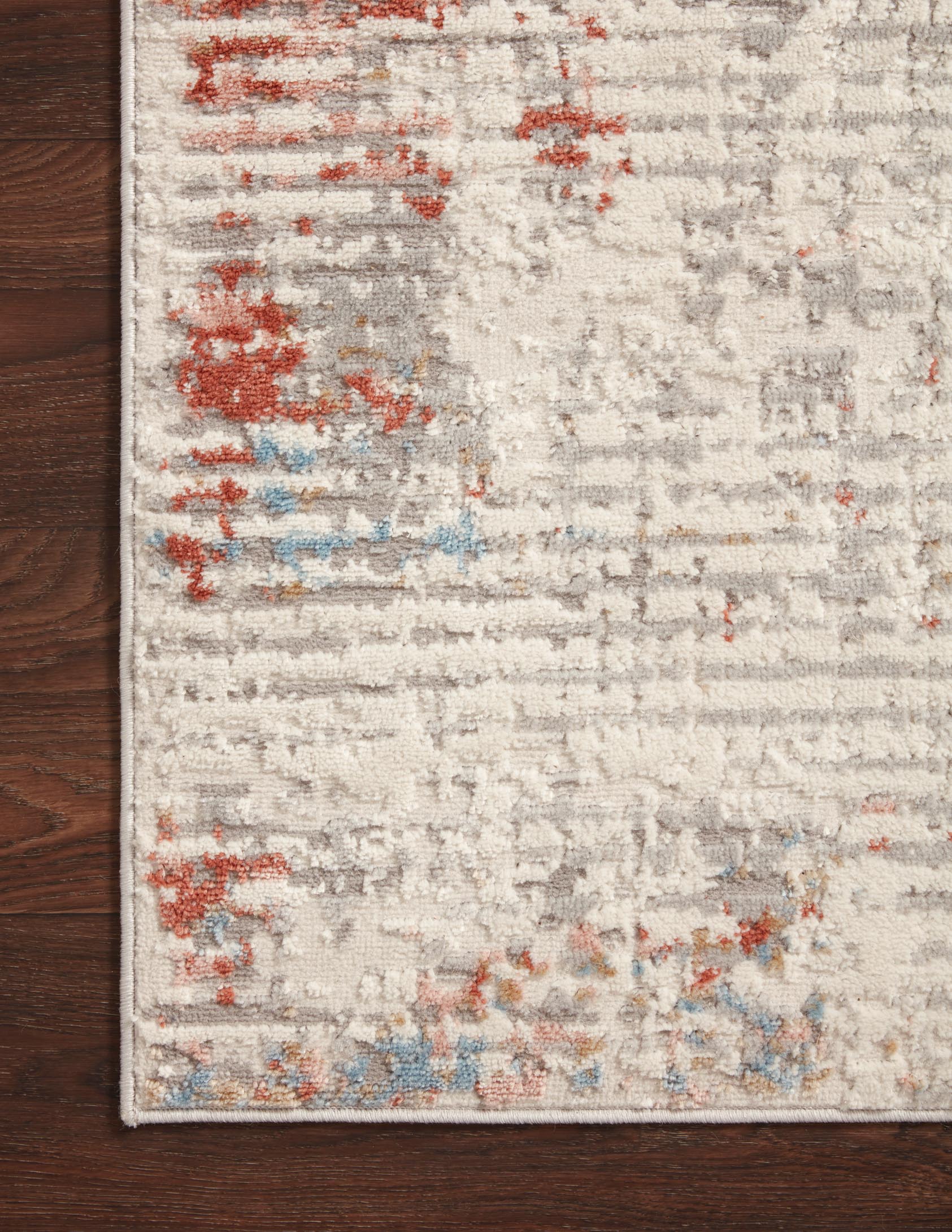 Ivory rug corner on dark wood floor with distressed red and blue abstract markings