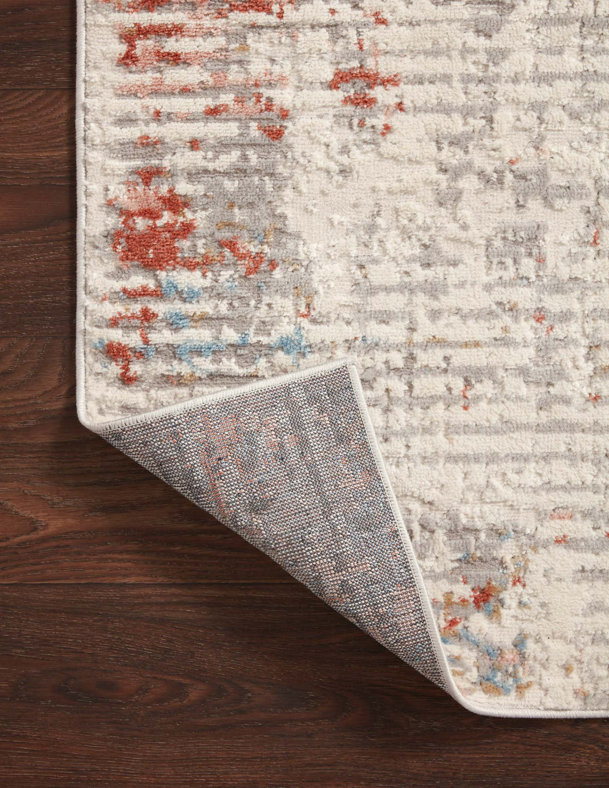 Ivory rug rolled back at the corner, showing texture and distressed red and blue pattern