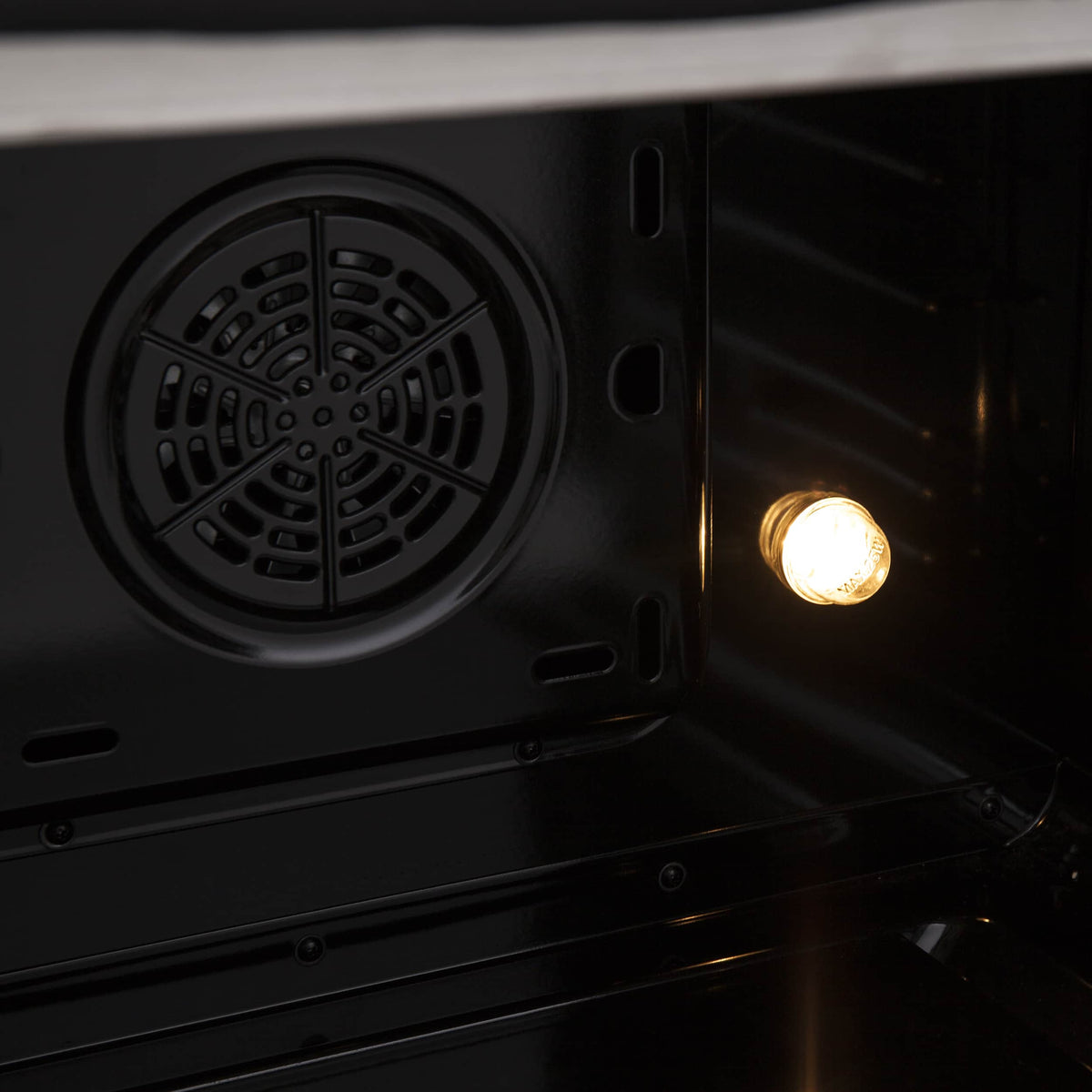 Dual fuel range oven interior with round convection fan vent and warm light