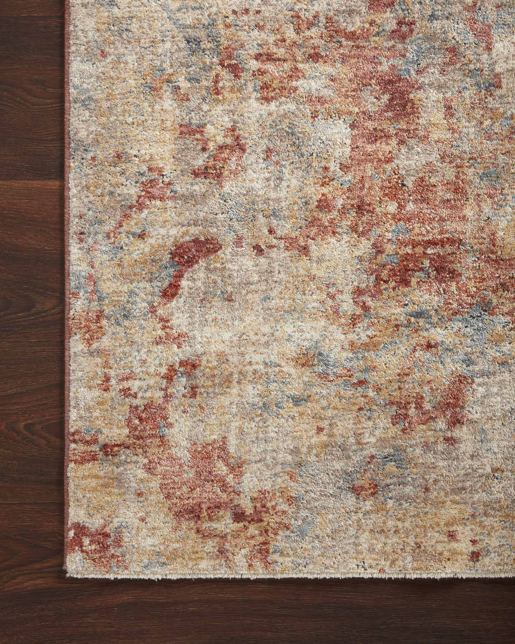 Abstract taupe and brick power-loomed rug with textured surface and border beside hardwood.