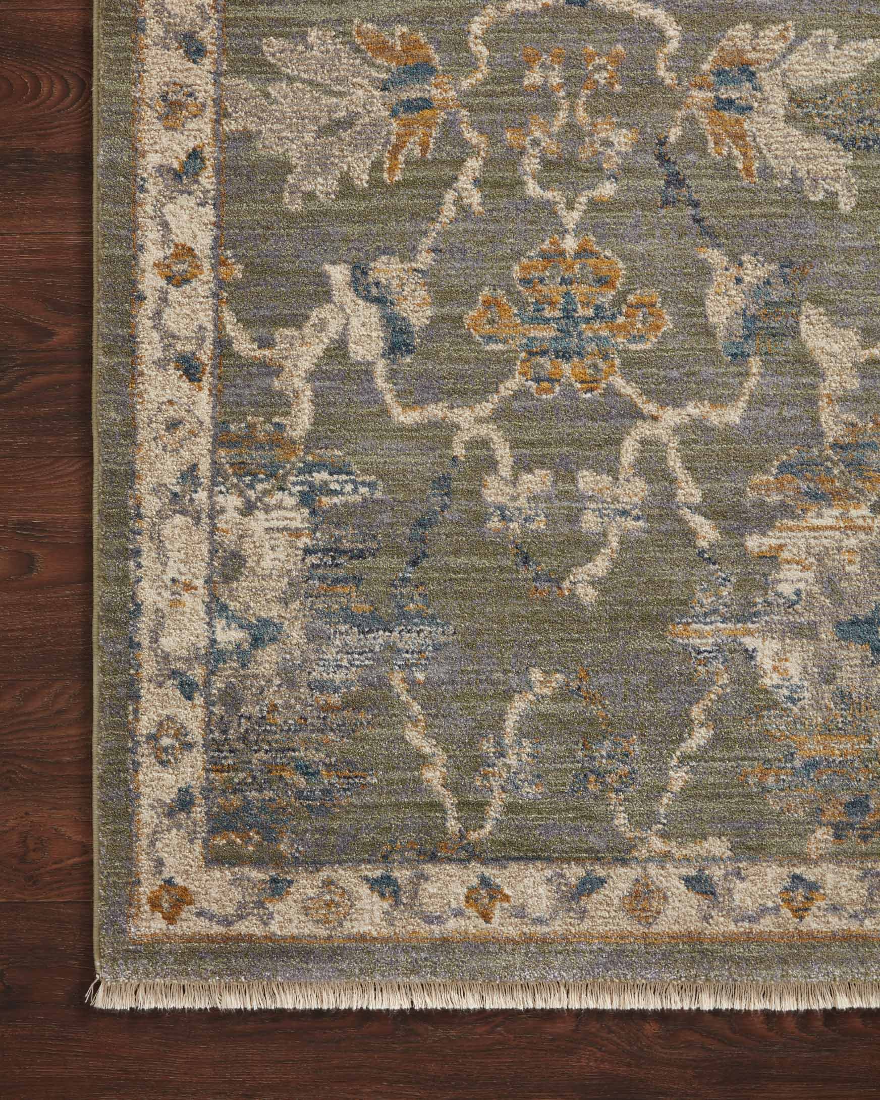 Close-up of sage and gold rug with detailed traditional motif pattern and fringed edge.
