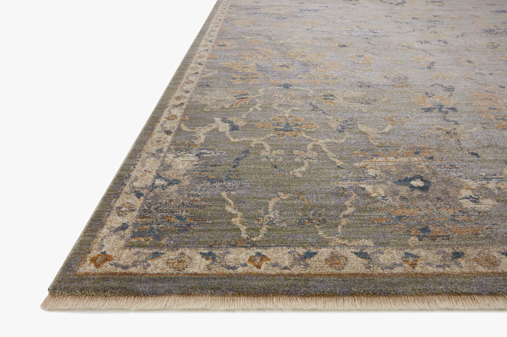 Corner of sage and gold distressed rug with ornate pattern and short fringe edge.