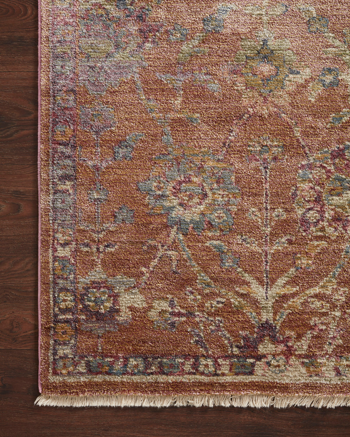 Corner view of terracotta rug with textured weave, ornate motifs, and short fringe