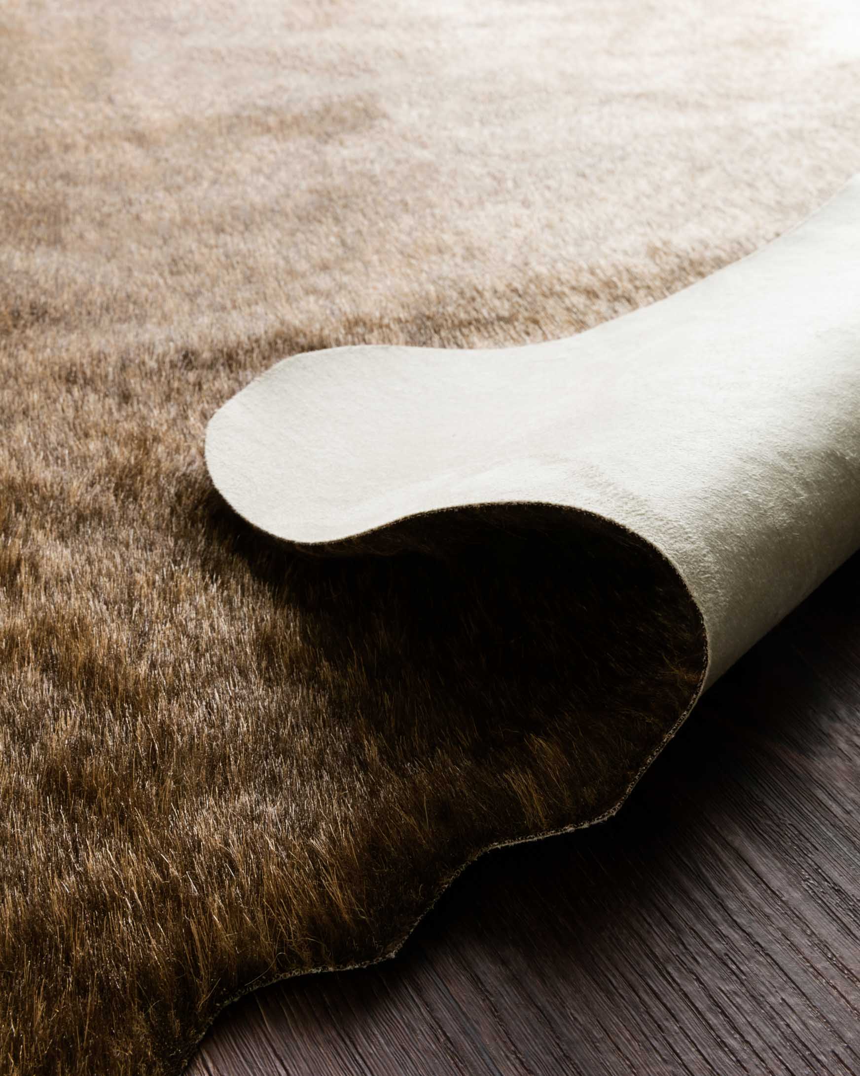 Corner detail of camel-brown and cream cowhide-style rug with curved bound edge