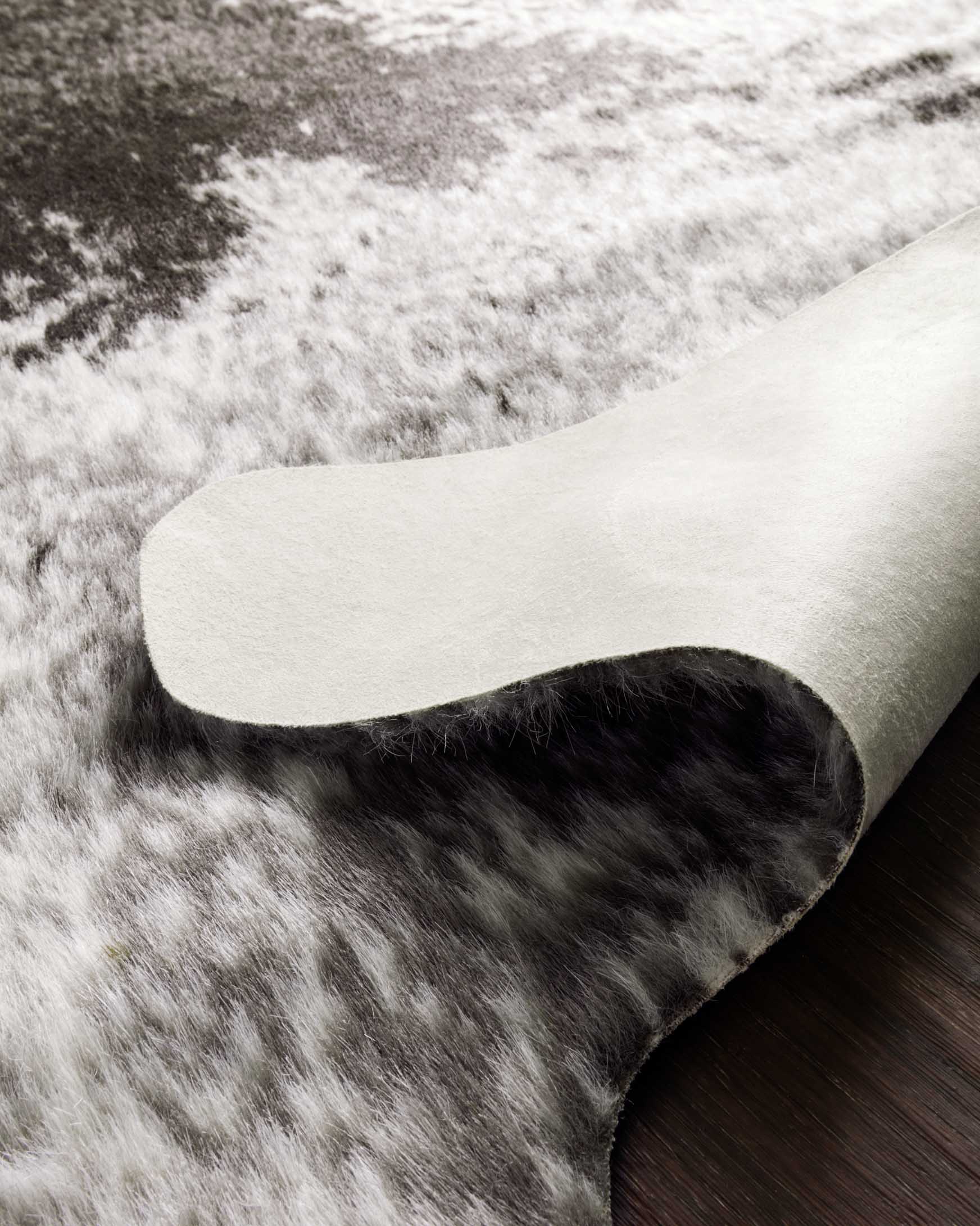 Ivory and charcoal rug with speckled texture, curved edge and folded pile detail