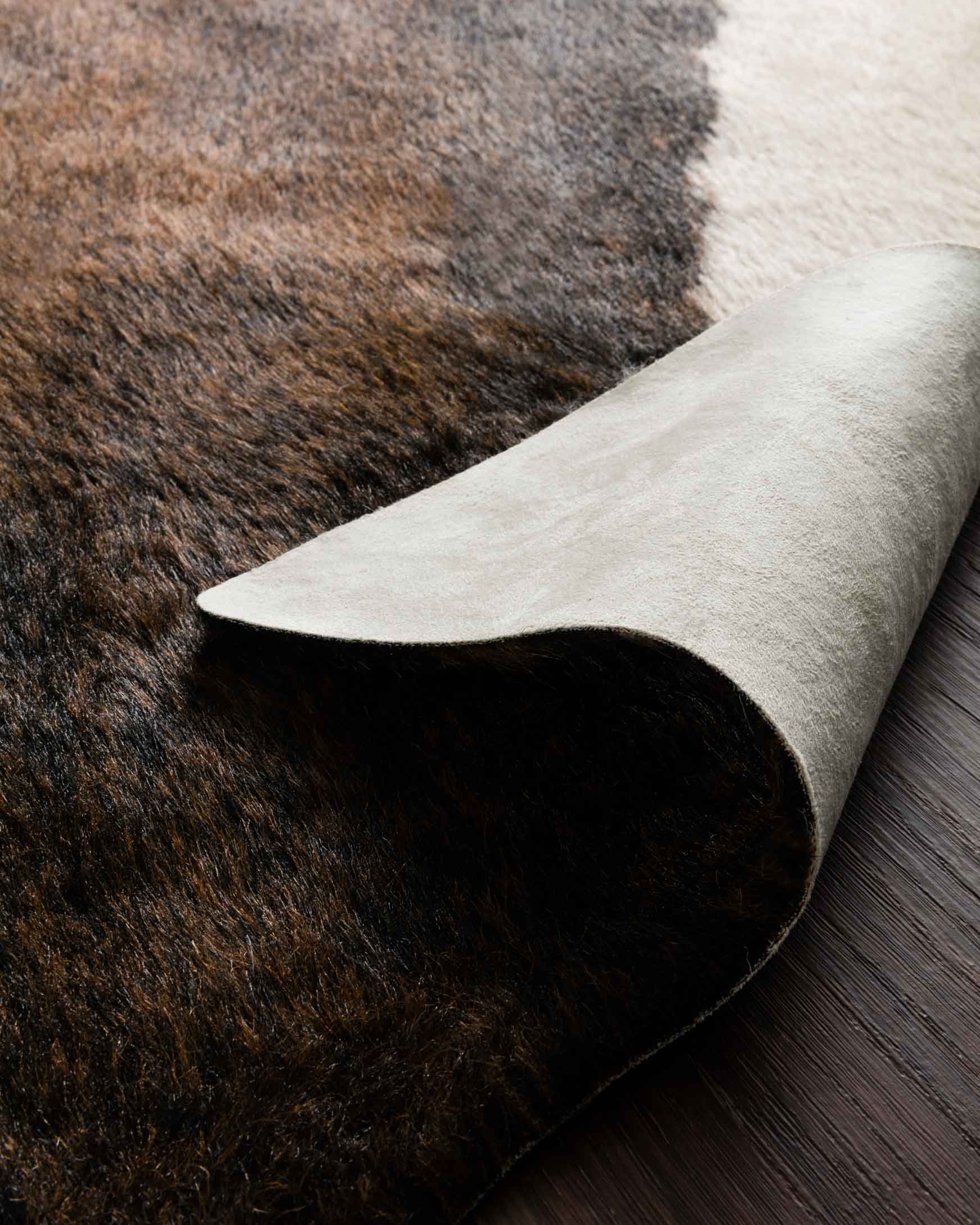 Edge of beige and brown cowhide-style rug, rolled with dark mottled underside