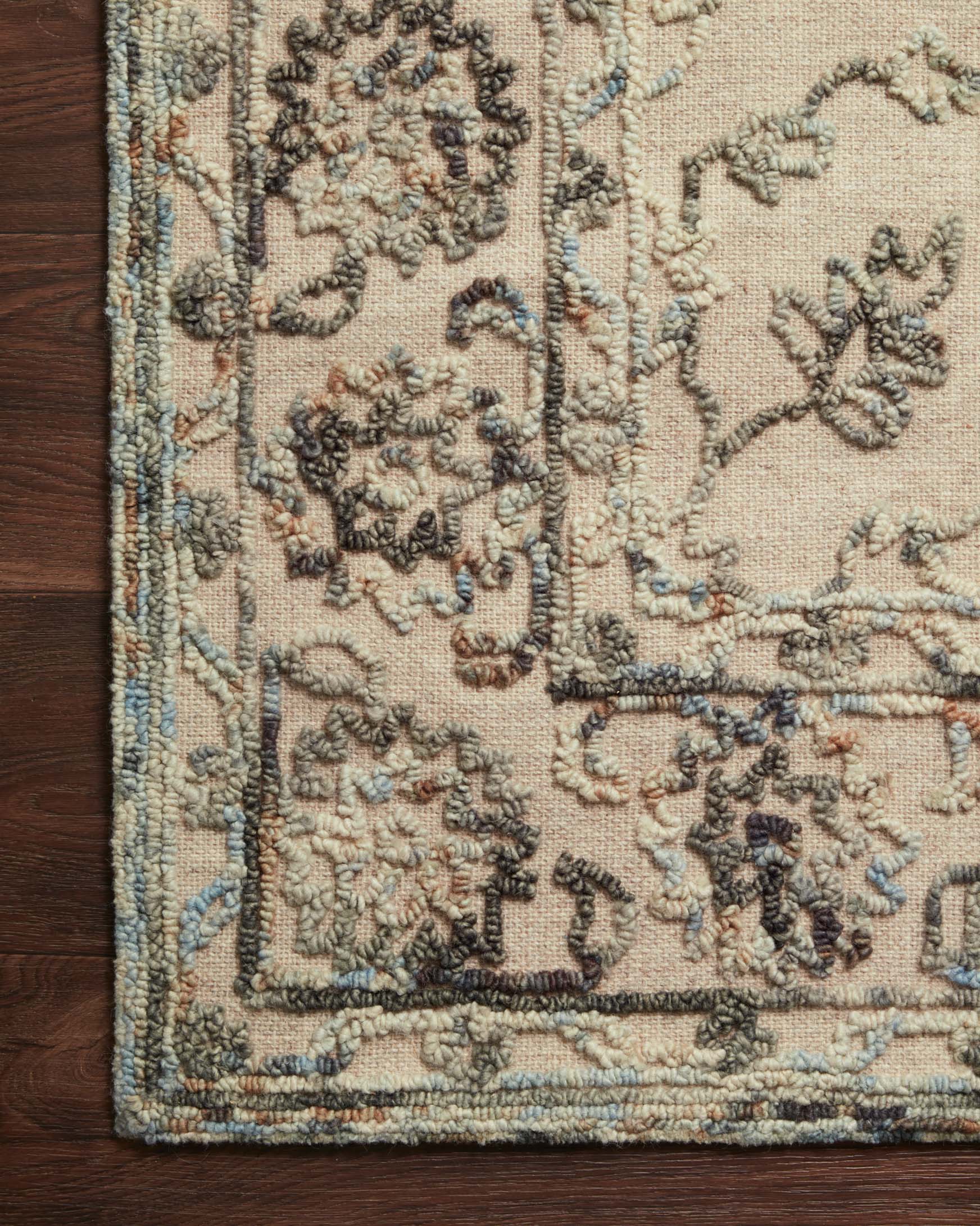 Close-up of grey and sky hooked rug with dense stitched motifs and border trim