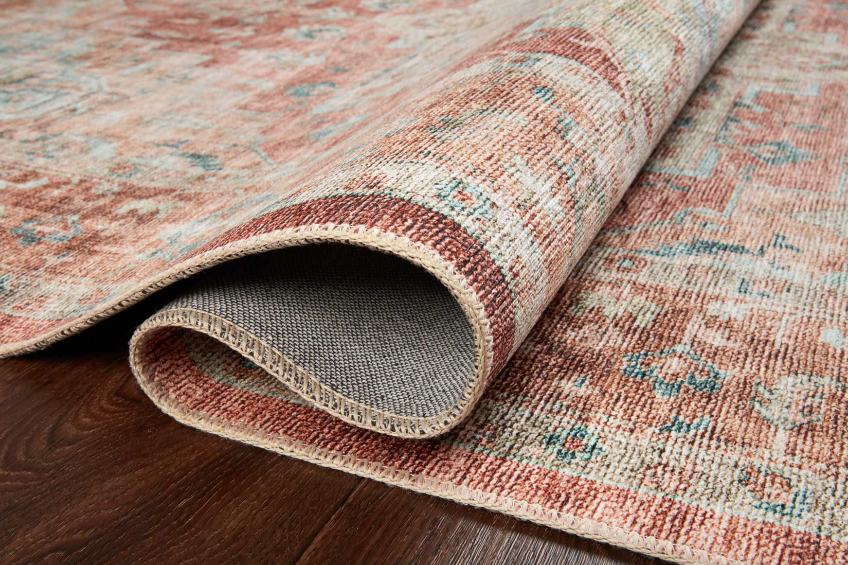 Rolled edge of terracotta and aqua rug showing textured surface and gray backing