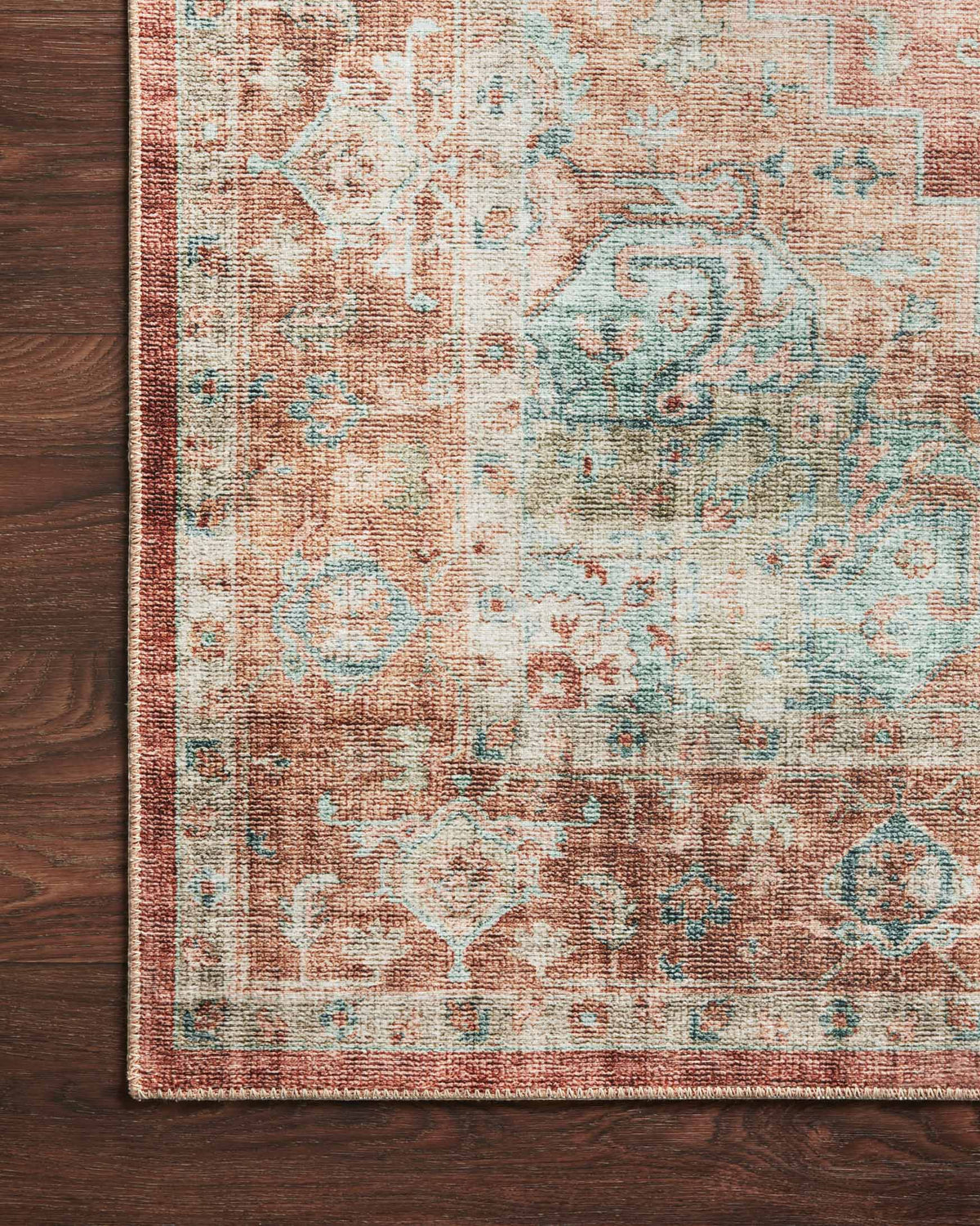 Close-up of terracotta and aqua traditional rug edge with detailed faded geometric motifs.