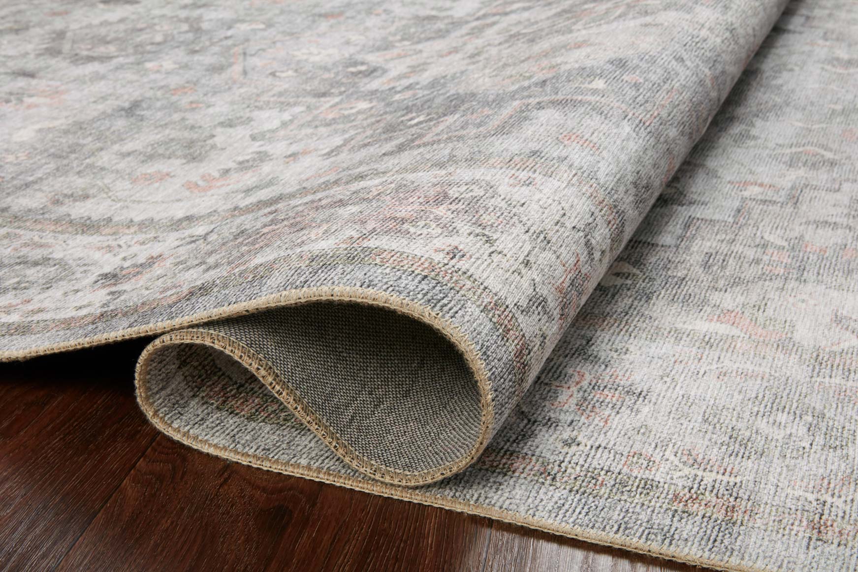 Rolled edge of light gray area rug showing woven texture and tan binding around edge.