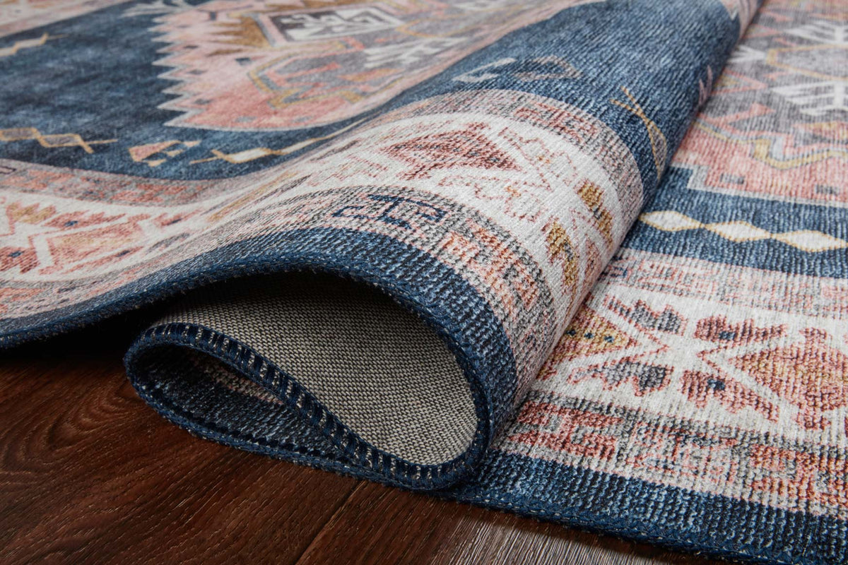 Rolled edge of denim blue area rug with geometric motif and stitched binding