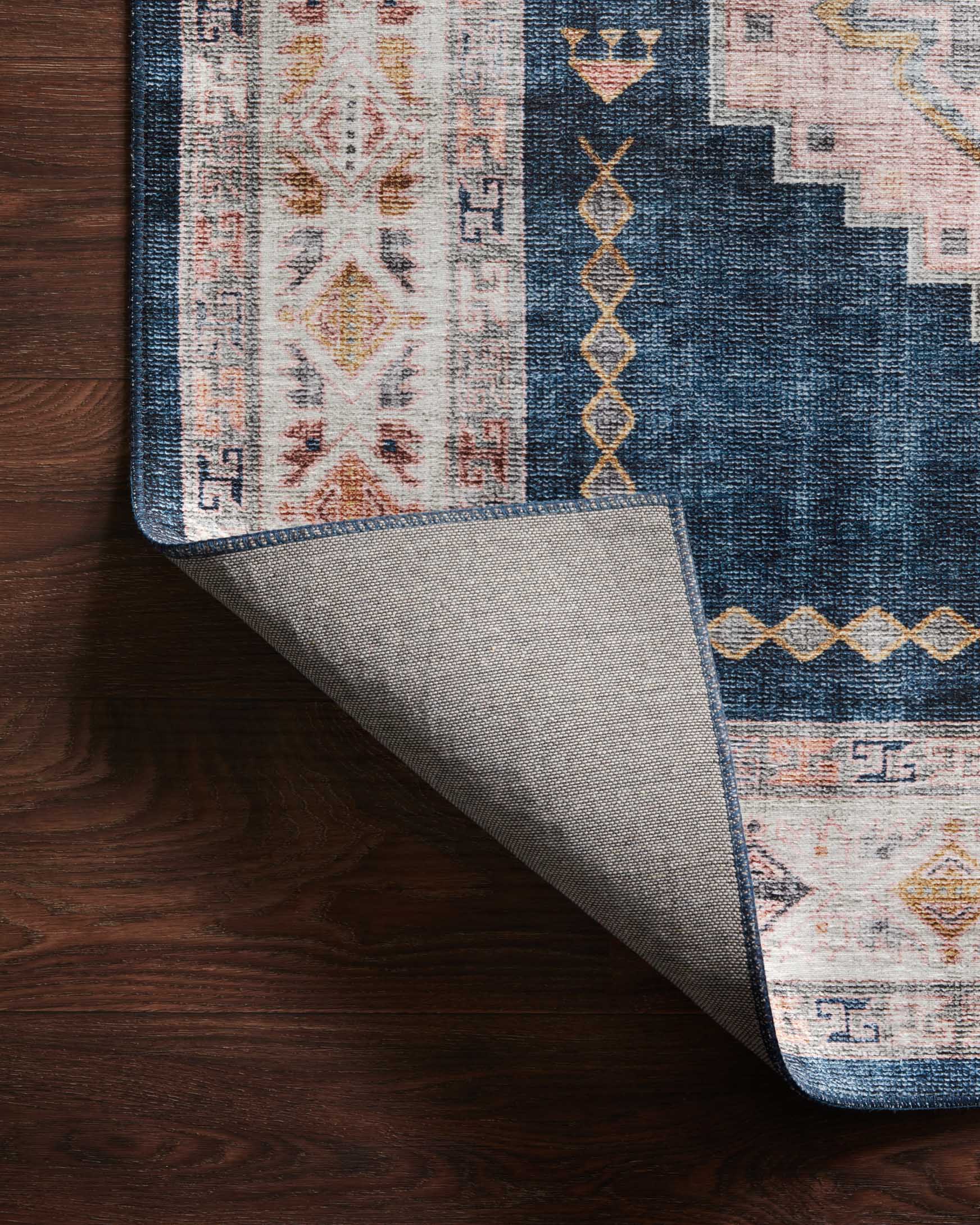 Folded corner of denim blue rug showing woven backing and geometric border