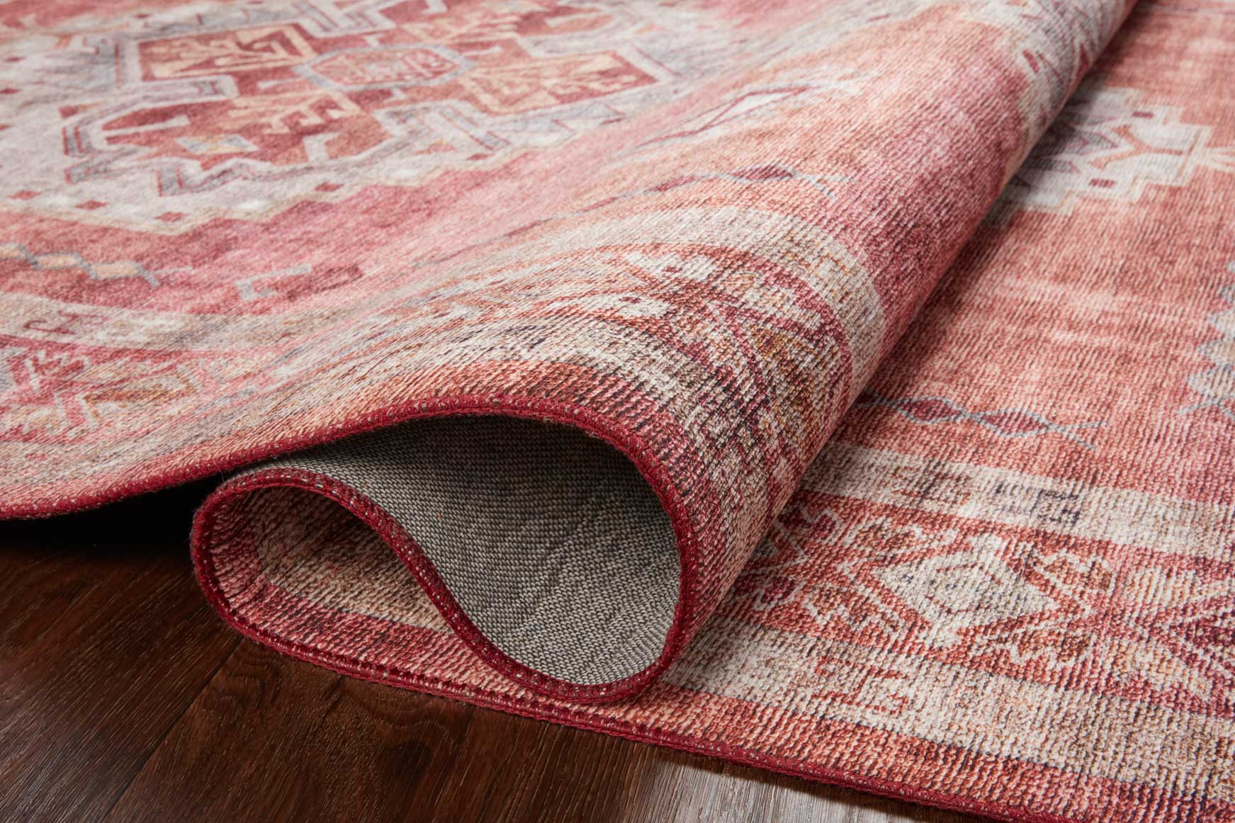 Rug edge detail showing rolled corner in rust red with beige backing underside.