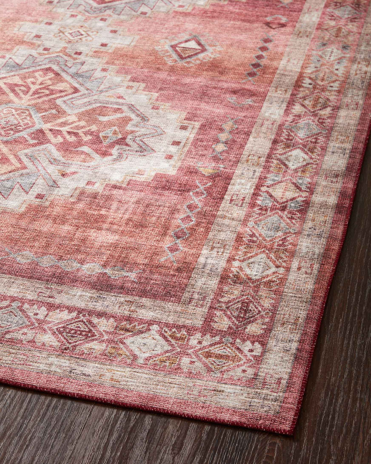 Corner close-up of rust red rug with ivory geometric border and diamond motifs.