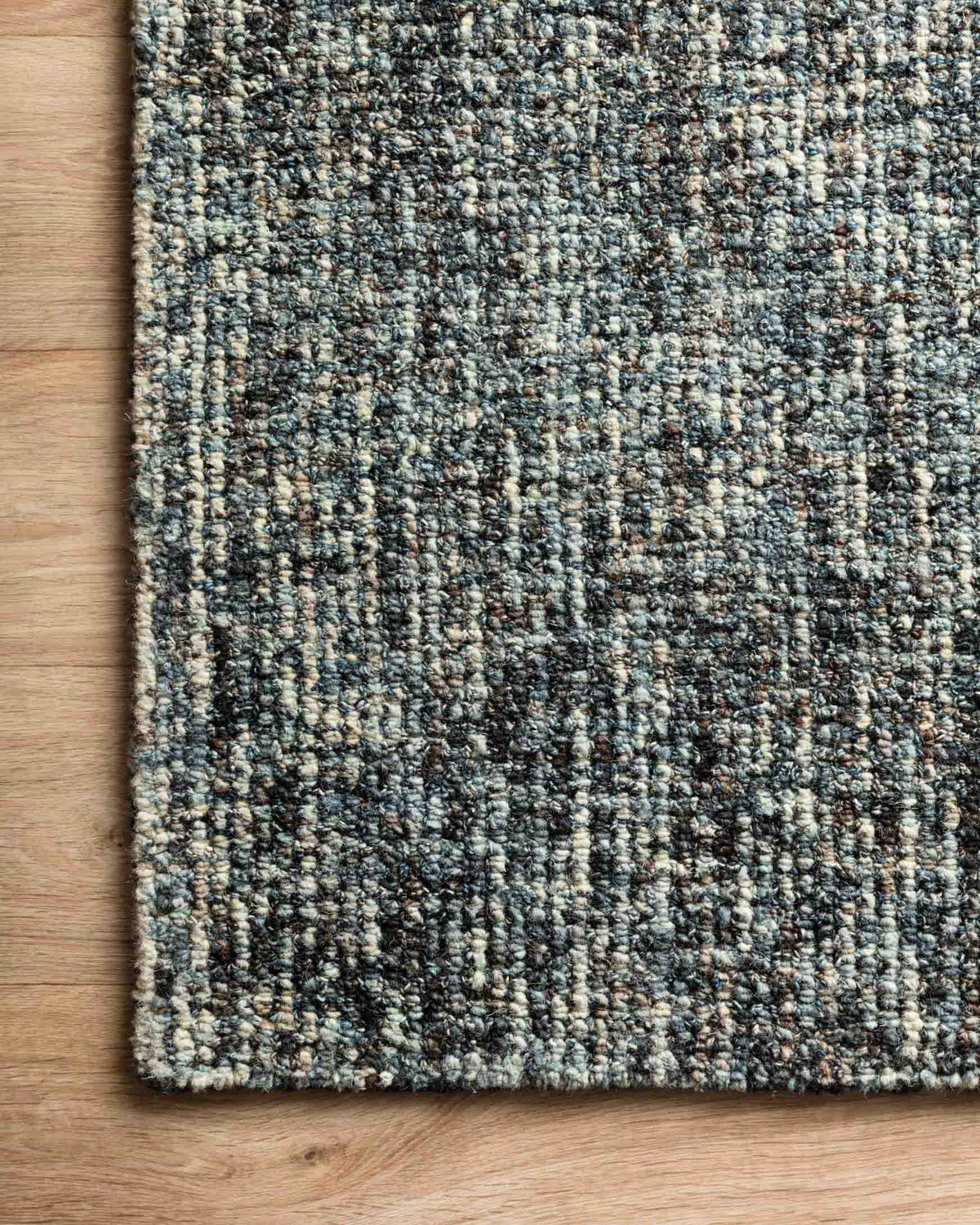 Denim-and-charcoal hand-tufted area rug edge detail on hardwood floor