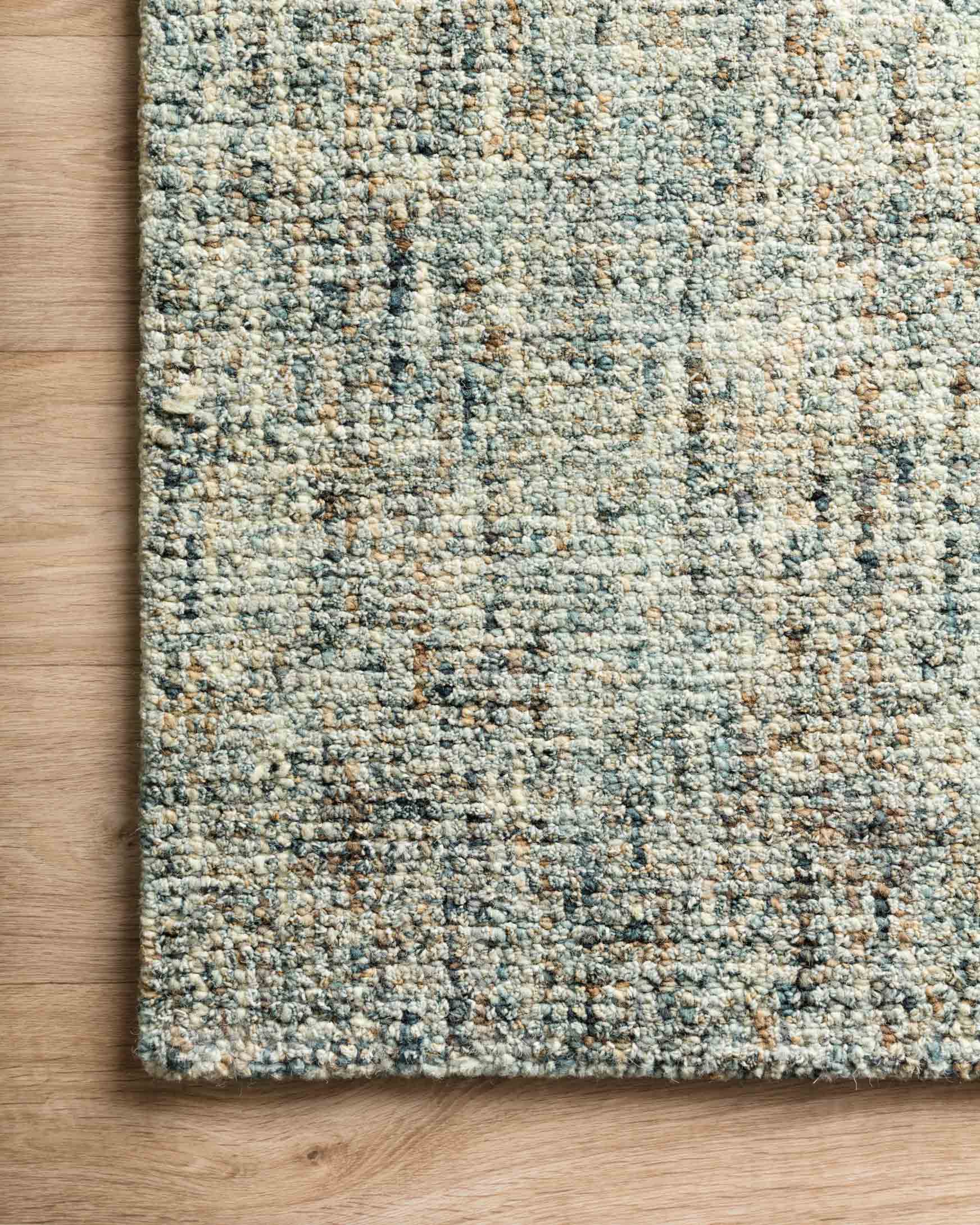 Hand-tufted area rug edge on wood floor, showing blue and sand speckled texture