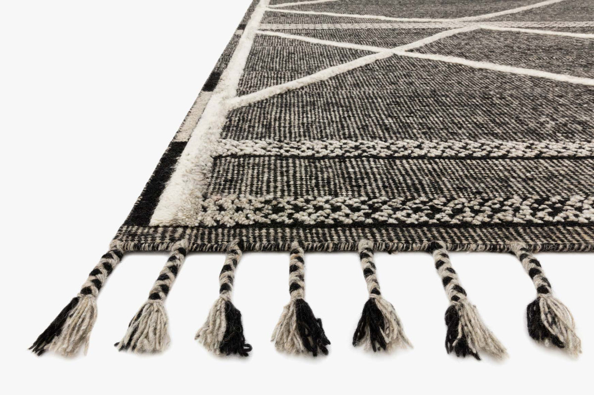 Corner of beige-and-charcoal rug with woven border and long tassel fringe