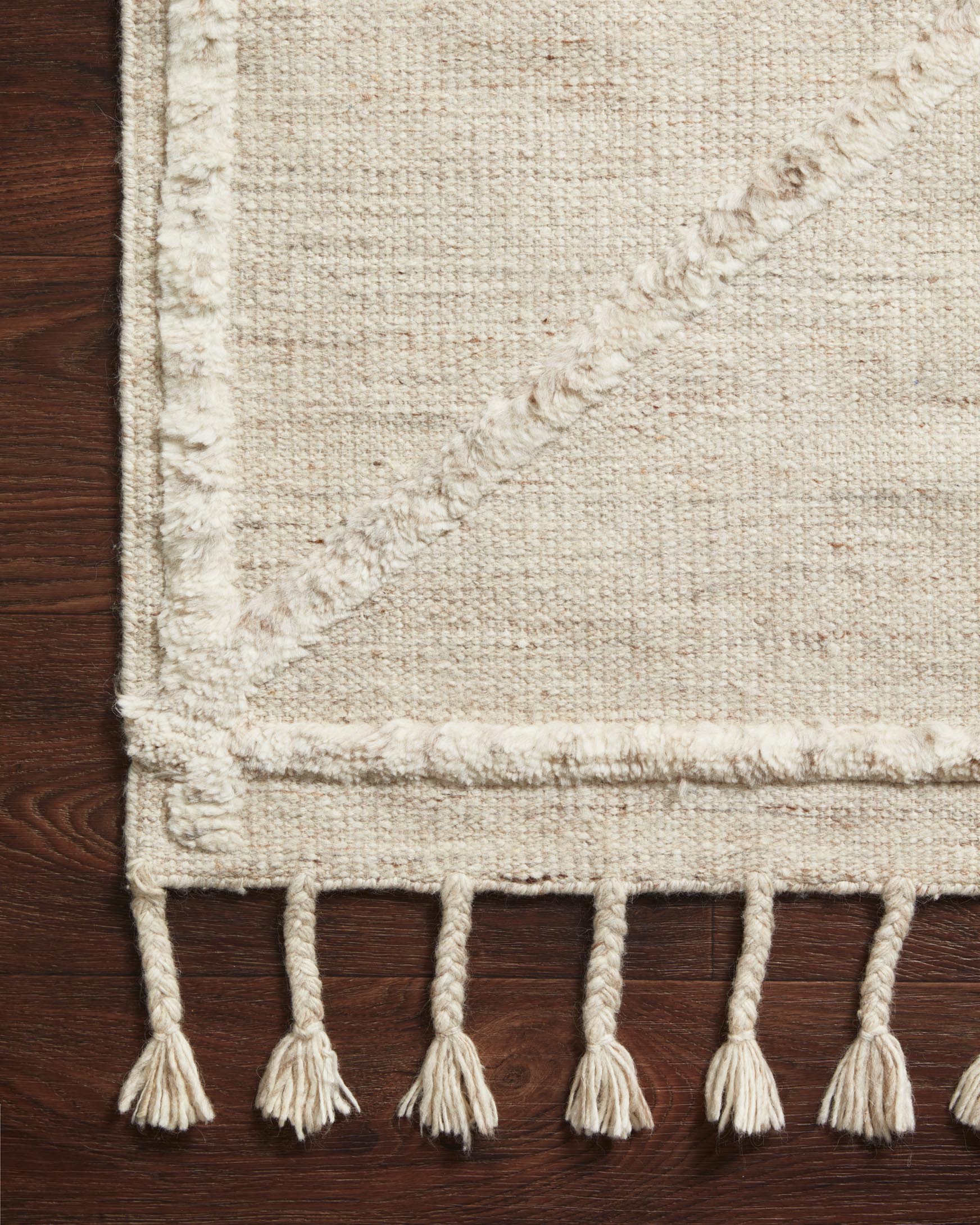 Beige and ivory area rug with short fringe tassels along the border, close-up corner