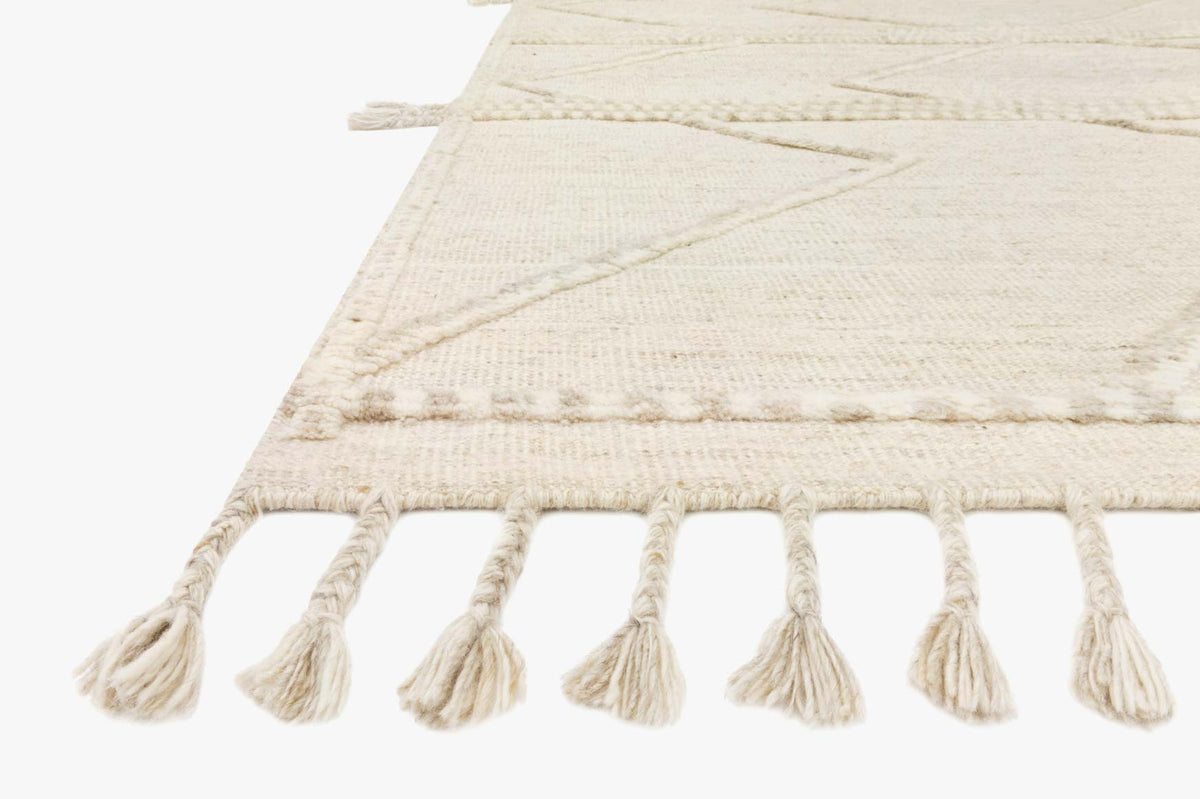Beige and ivory rug corner with braided border and short tassel fringe, angled close-up