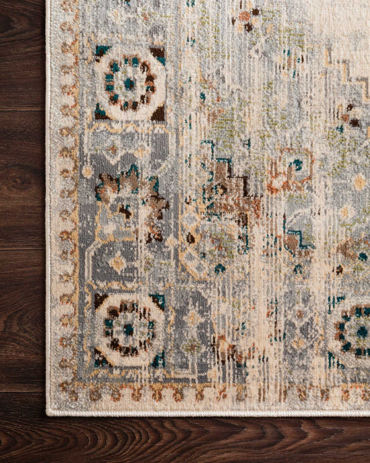 Corner view of oatmeal and silver rug with distressed medallions and teal geometric accents