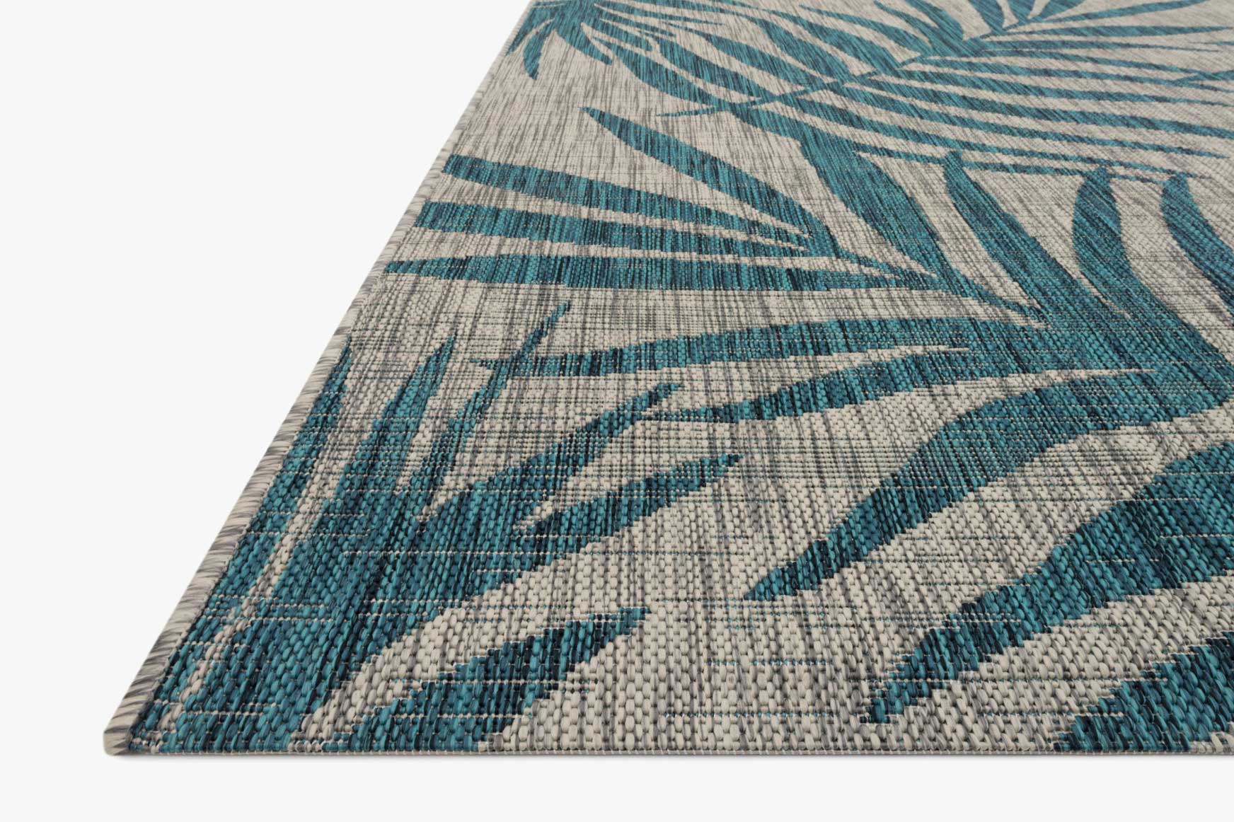 Corner view of indoor/outdoor rug with grey weave and aqua palm leaves