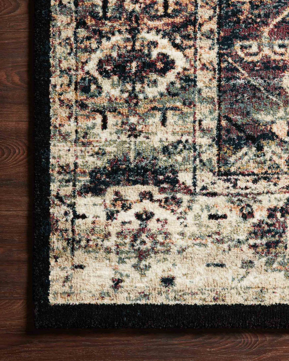 Corner view of power-loomed rug with cream center, dark navy border, and multicolor distressing