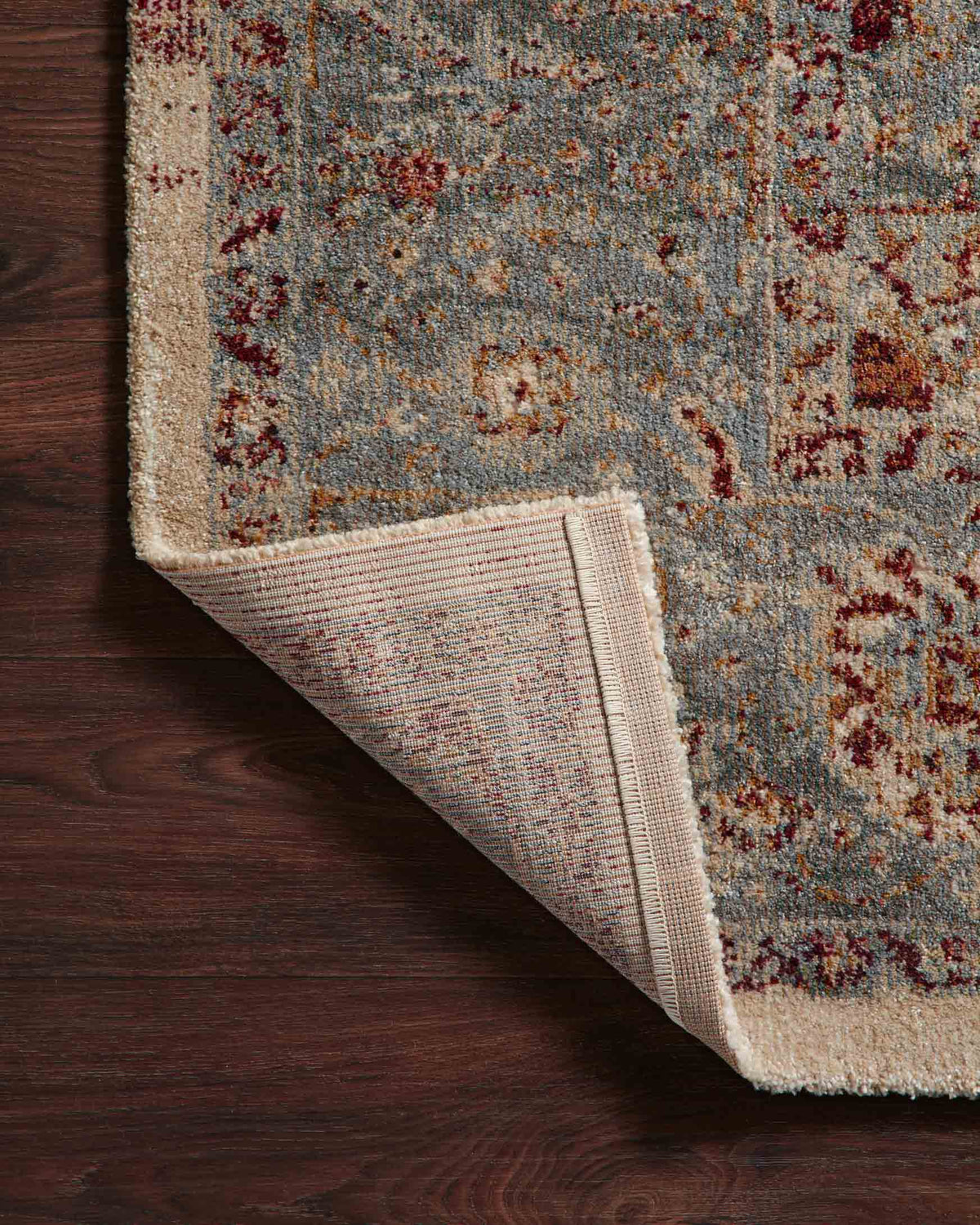 Corner view of slate blue rug with brick-red motifs and beige backing