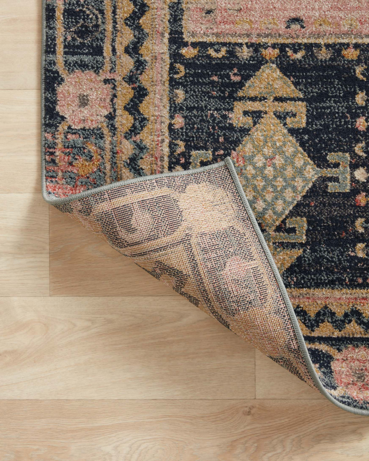 Rug corner with woven edge texture showing rose pink and dark navy pattern.