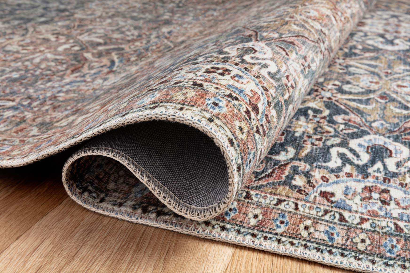 Rolled edge of traditional rug showing patterned face and dark backing underneath