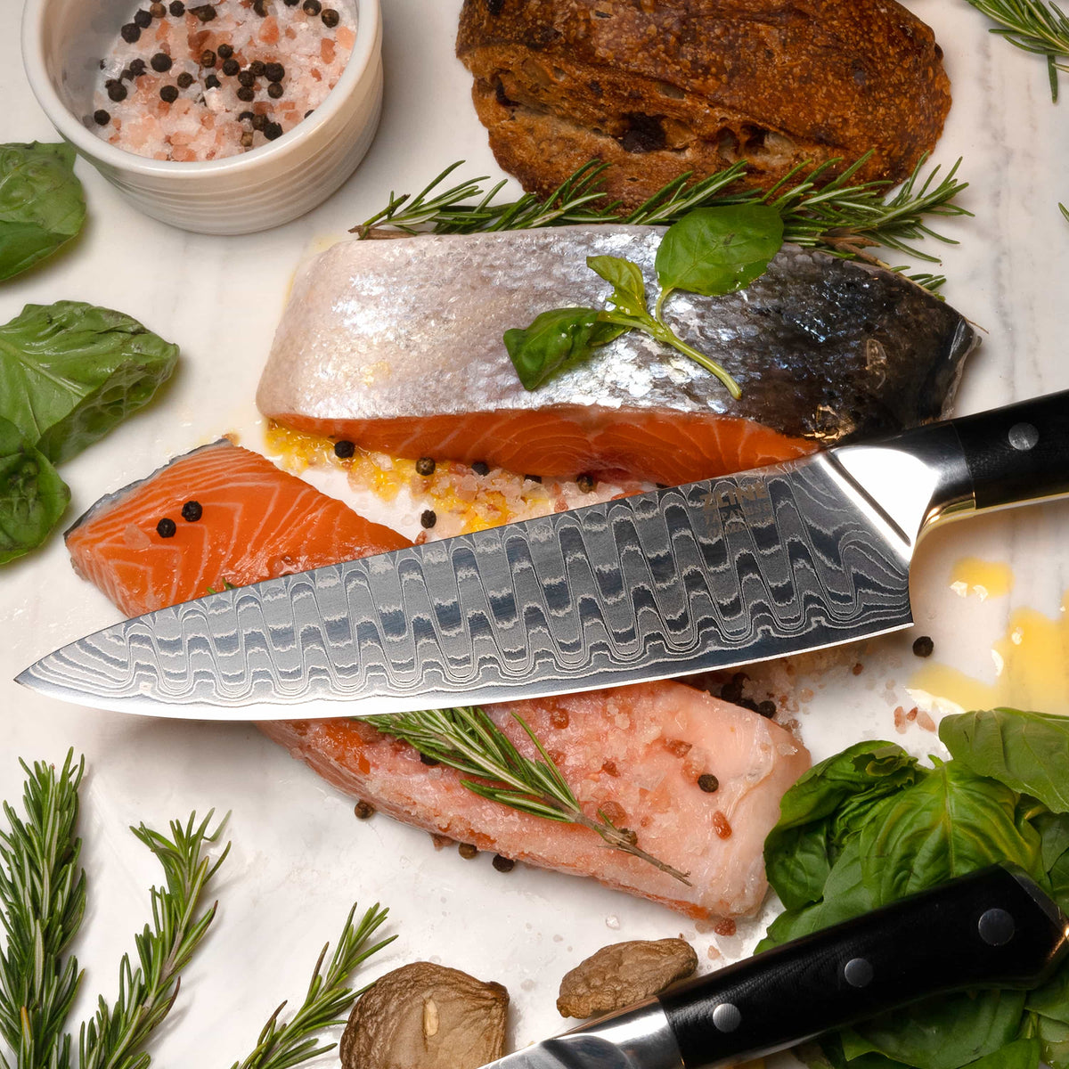 Damascus steel chef’s knife on cutting surface, black handle with rivets and patterned blade