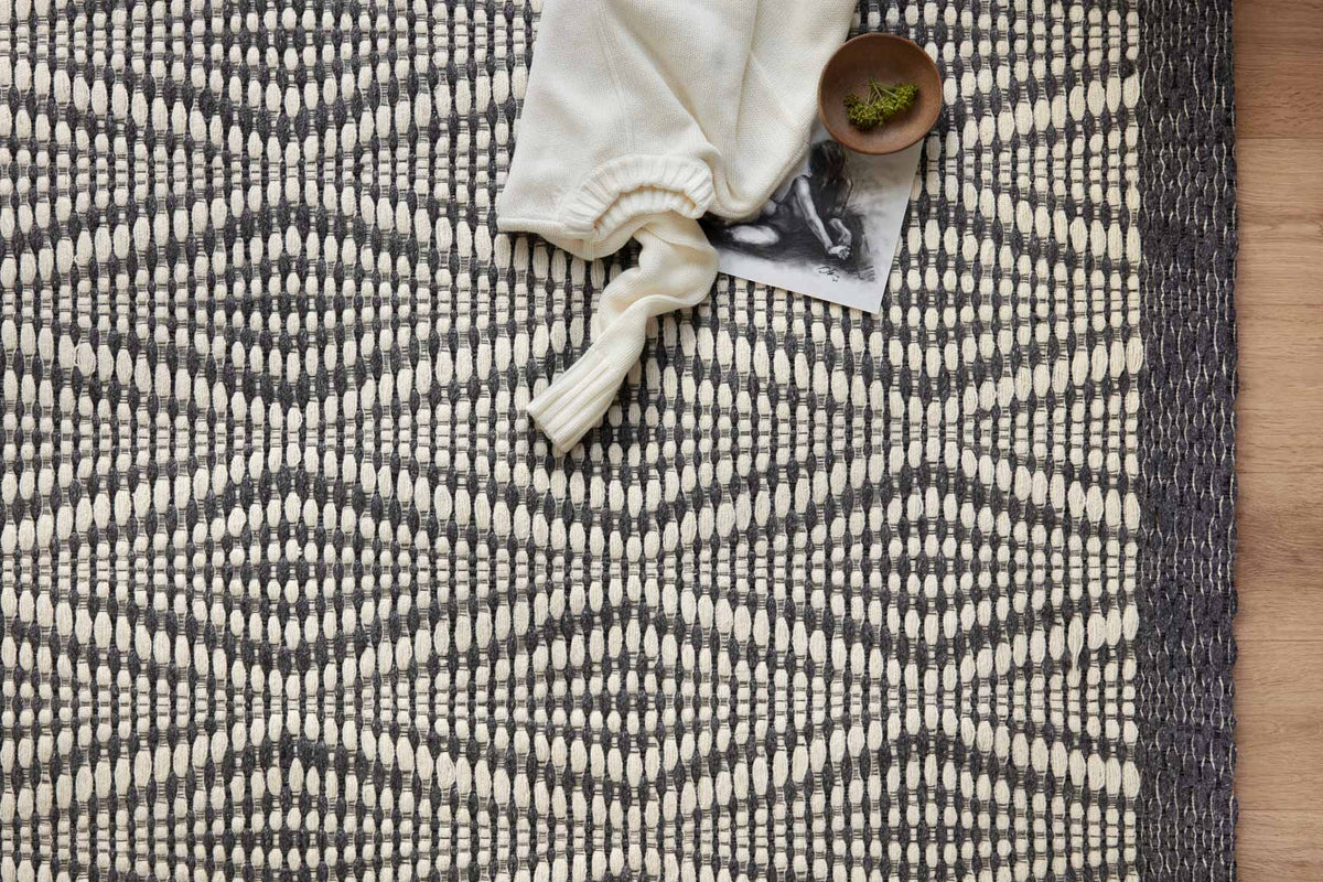 Close-up of ivory and charcoal rug texture with diamond pattern and short fringe